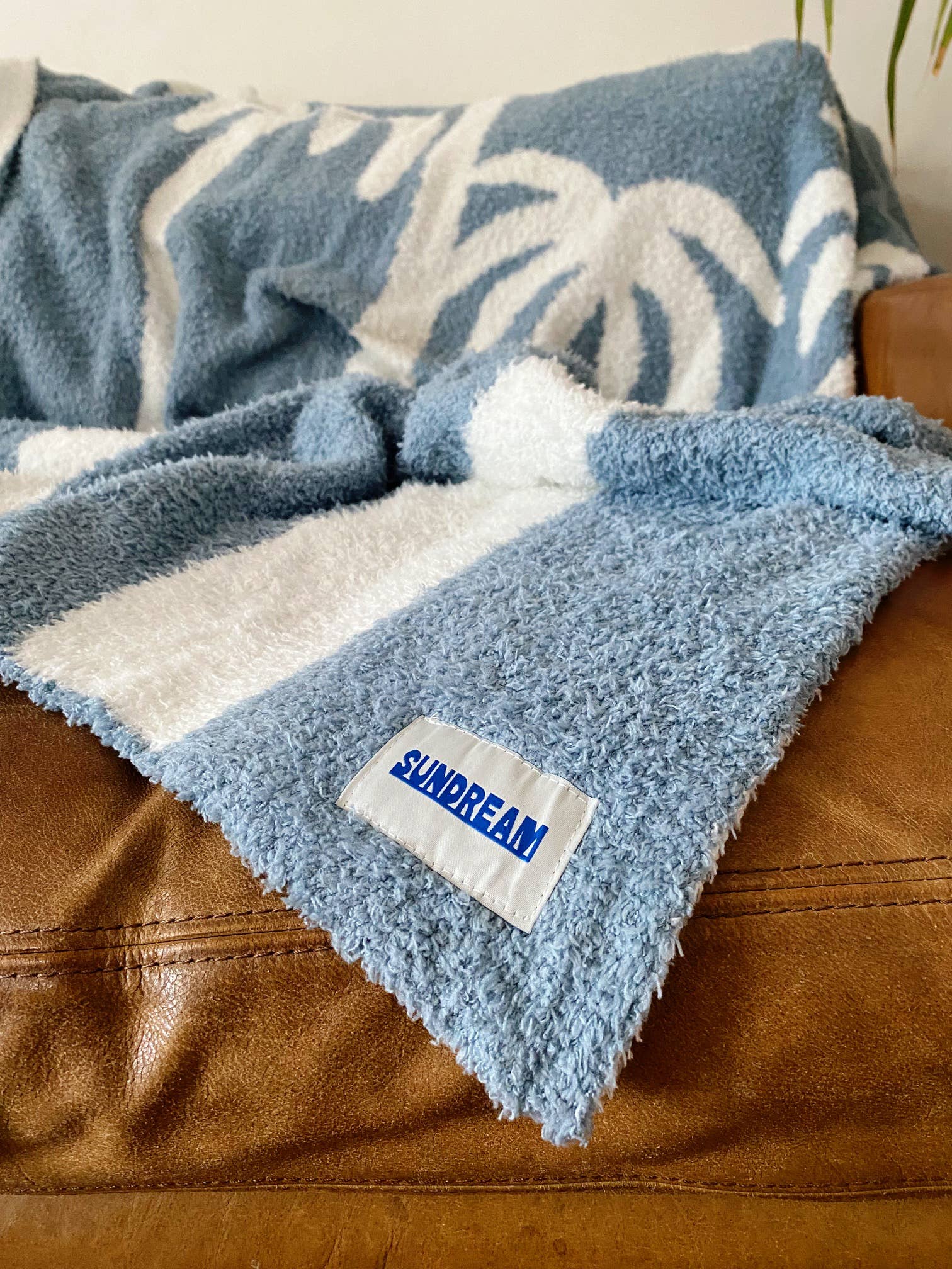 Soft chambray blue plush throw with palm tree design, perfect for cozying up or adding a beachy touch to any space.