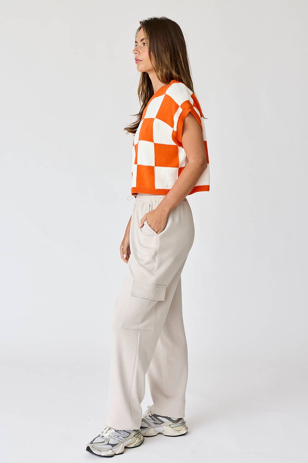 Woman wearing an orange and white loose-fit checker knit top with beige pants.