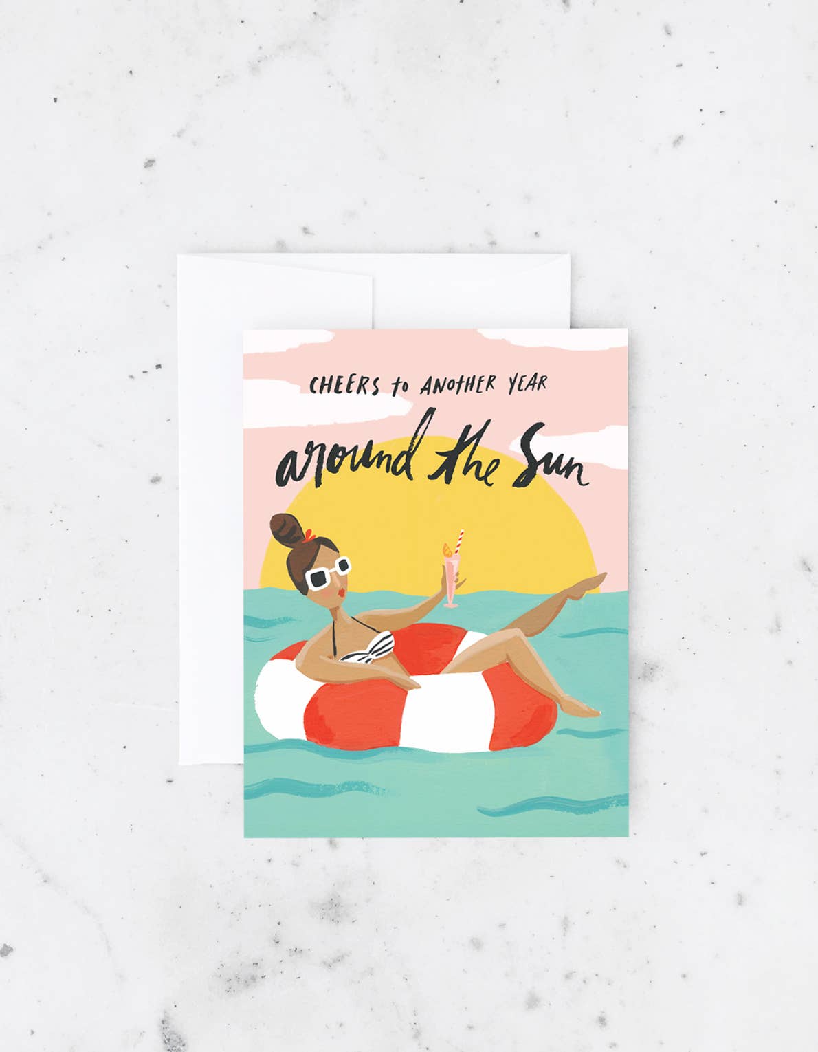 Birthday card with an illustration of a woman in a floatie holding a drink with the words “Cheers to another year around the sun”.