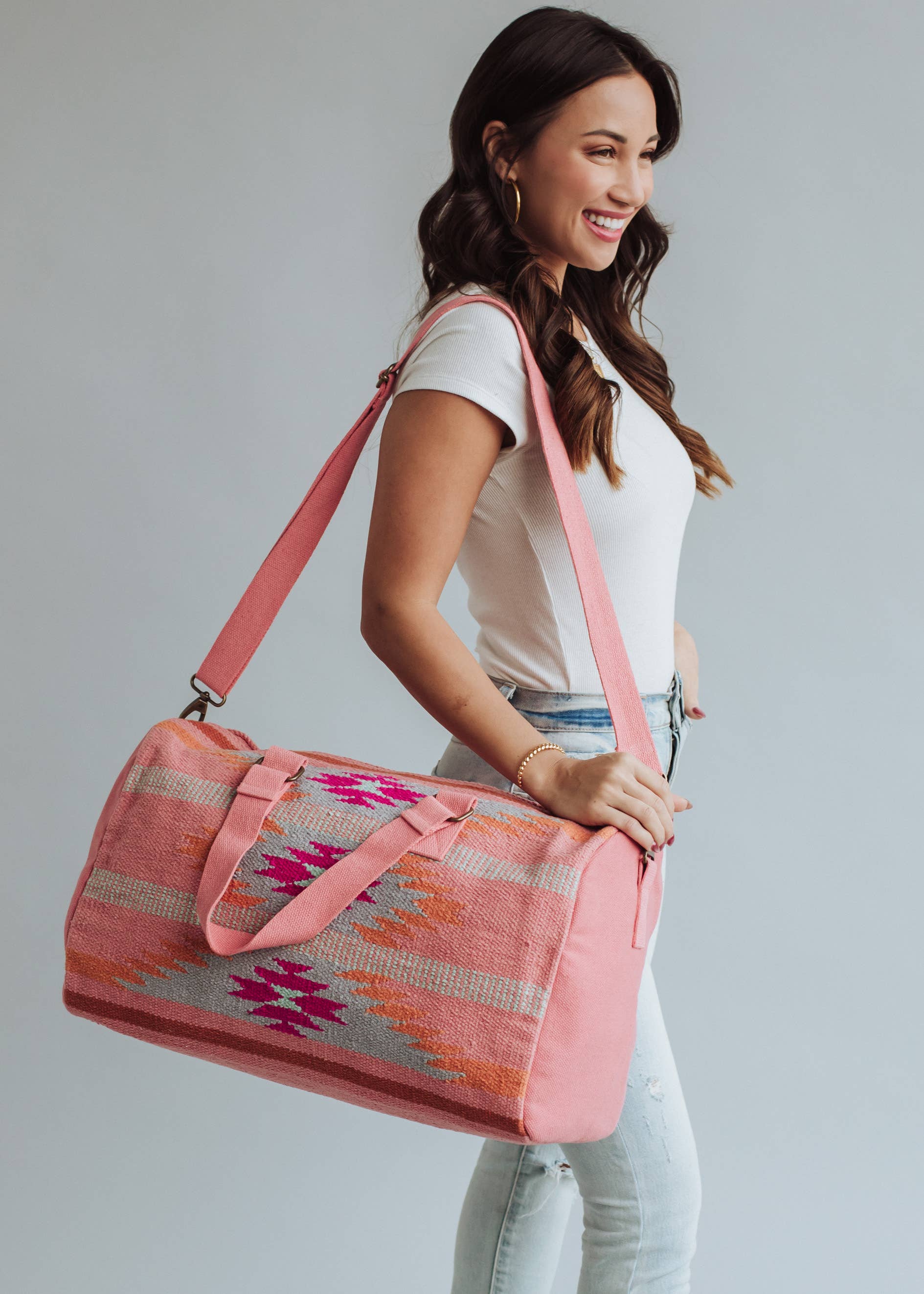 Woman holding a pink and orange woven weekender duffel bag with fuchsia geometric design