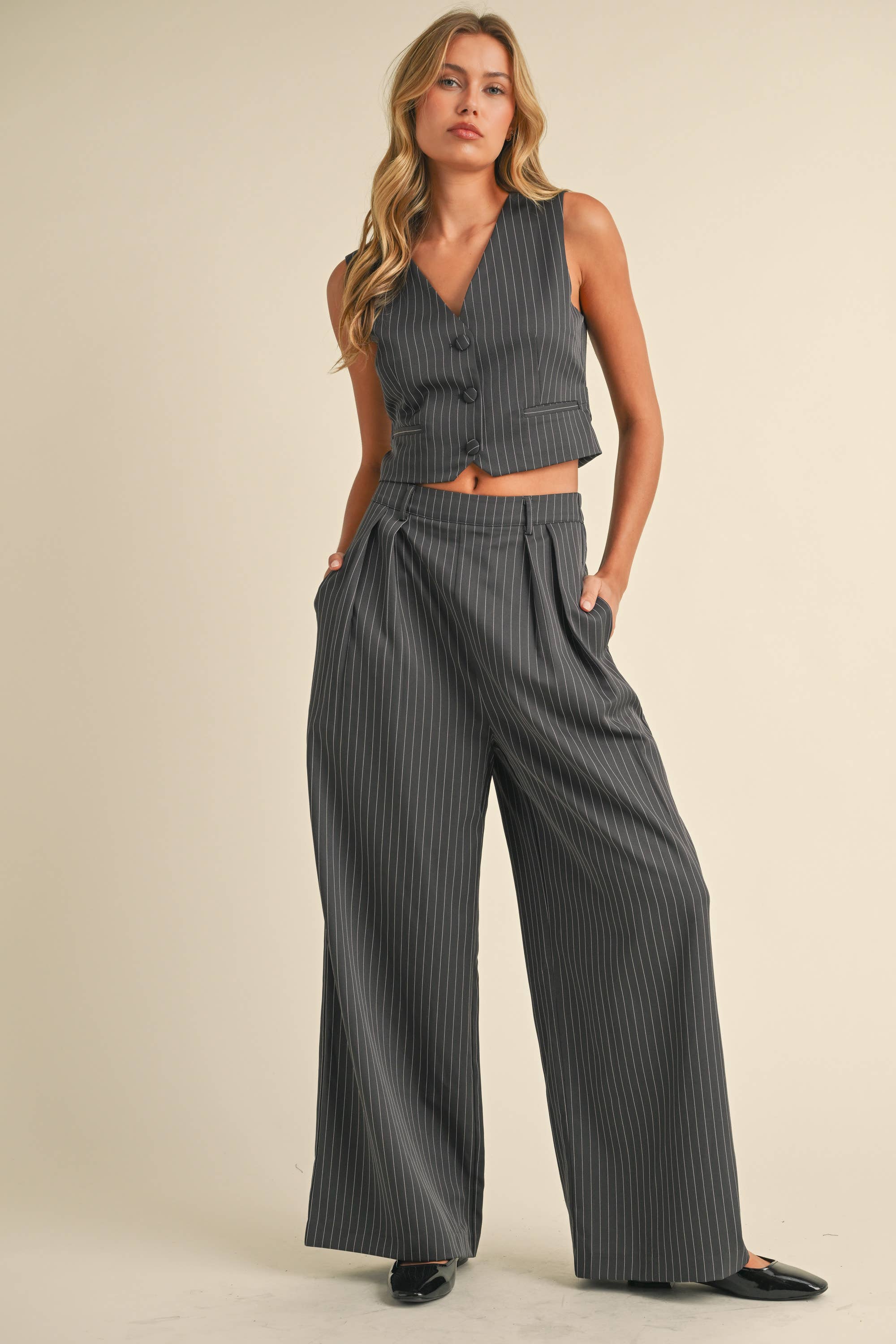 Woman wearing a sleeveless pinstriped vest and matching high-waisted wide-leg trousers.