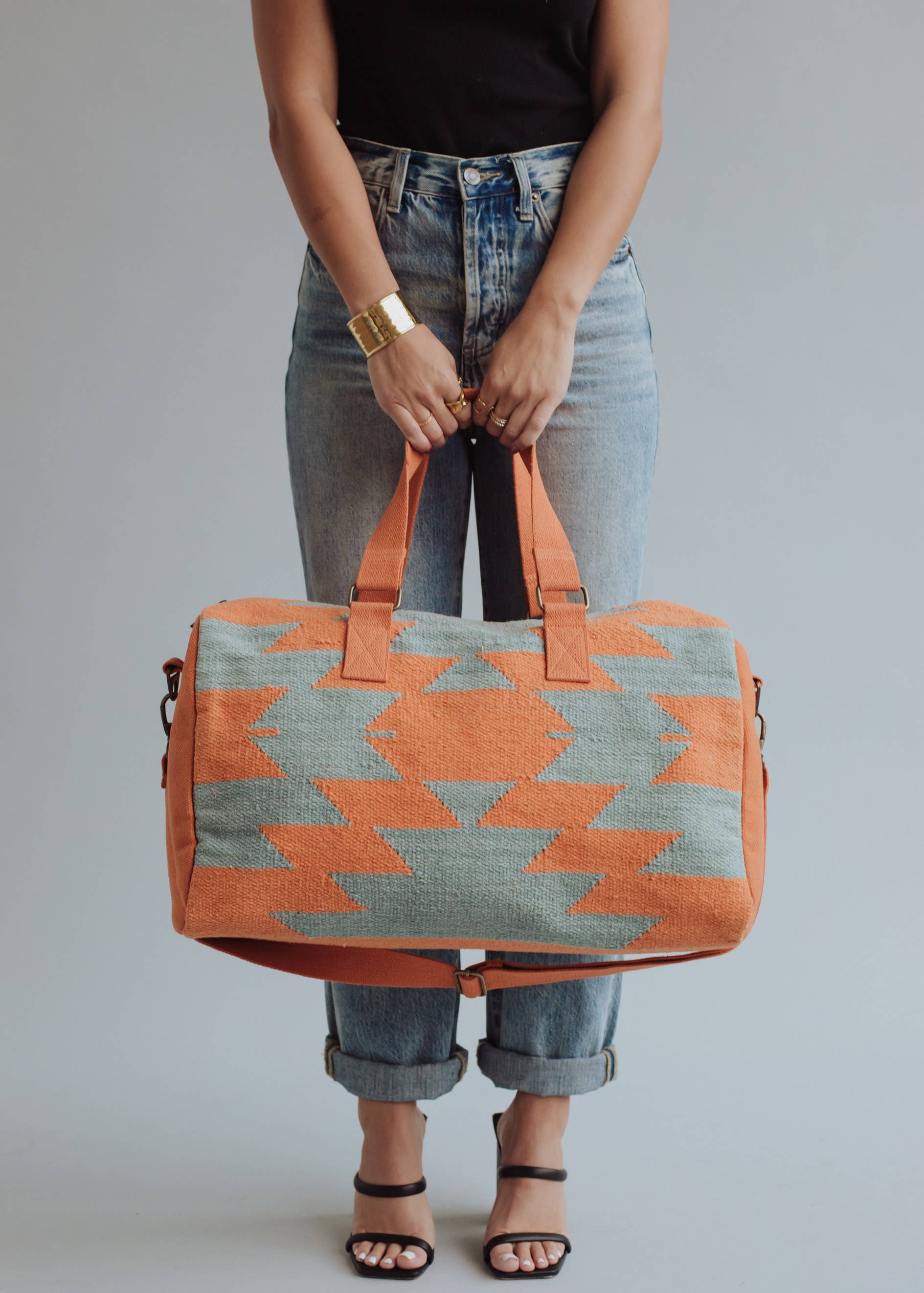 Wool woven orange and sage green weekender bag with geometric pattern, held by woman in jeans and black top