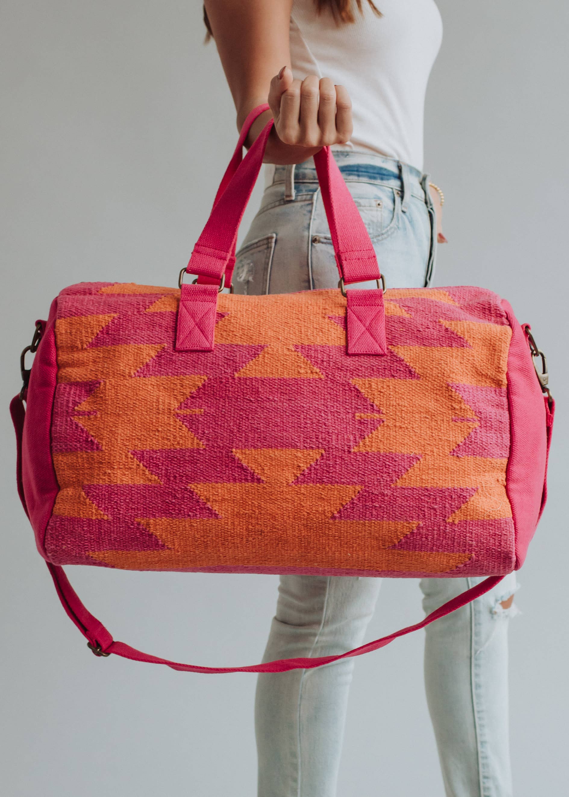 Bright orange and magenta woven weekender bag with geometric pattern, held by a woman in jeans
