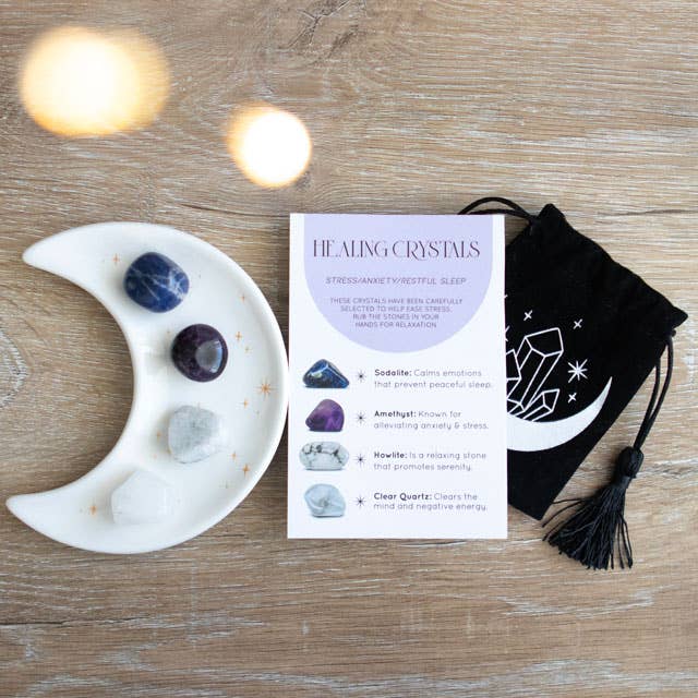 Stress Healing Crystal Set with Sodalite, Amethyst, Howlite, and Clear Quartz tumblestones on a crescent moon trinket dish, alongside a matching information card and printed drawstring pouch.
