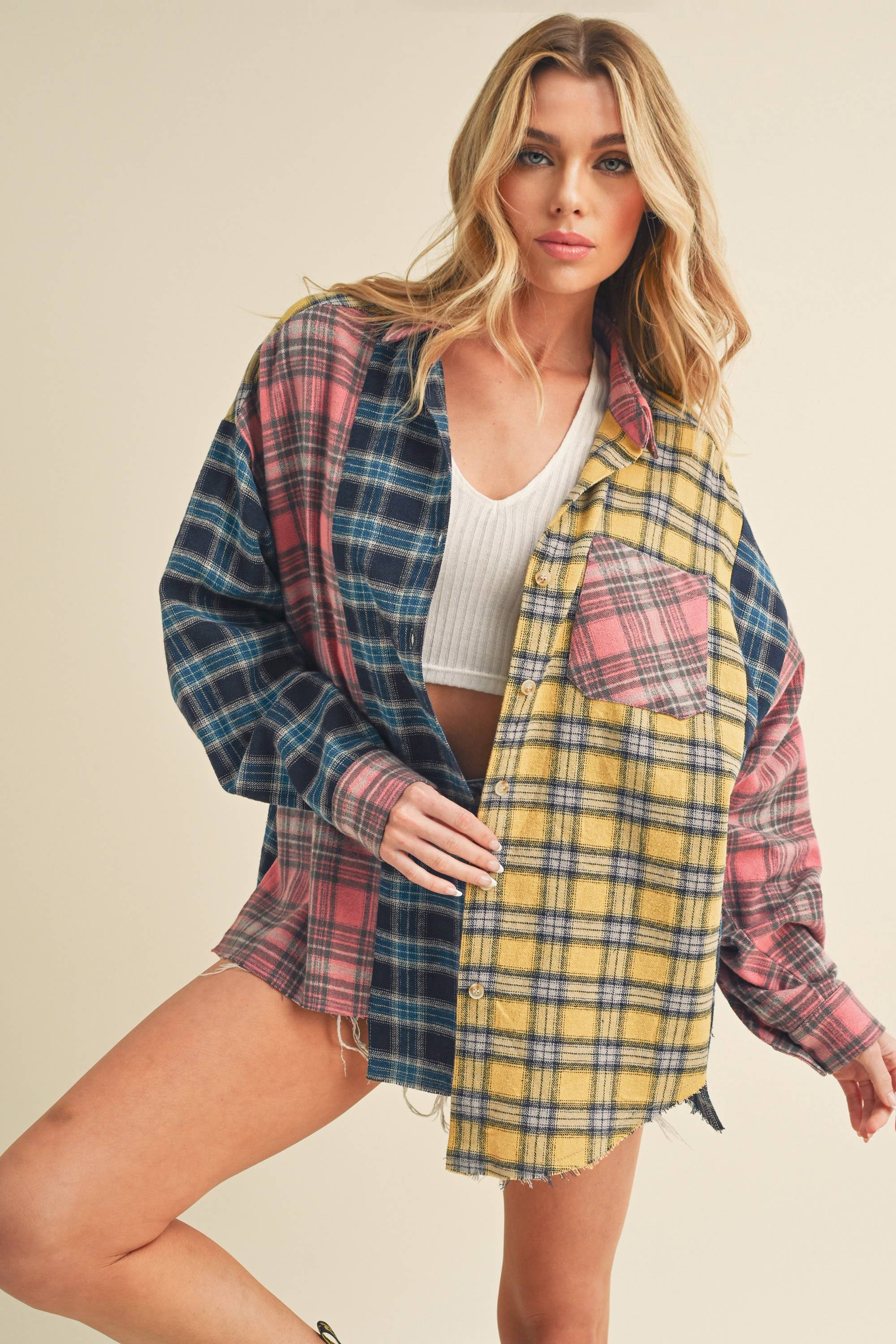Woman wearing an oversized plaid colorblock flannel shirt in pink, yellow, and navy tones with raw hems.