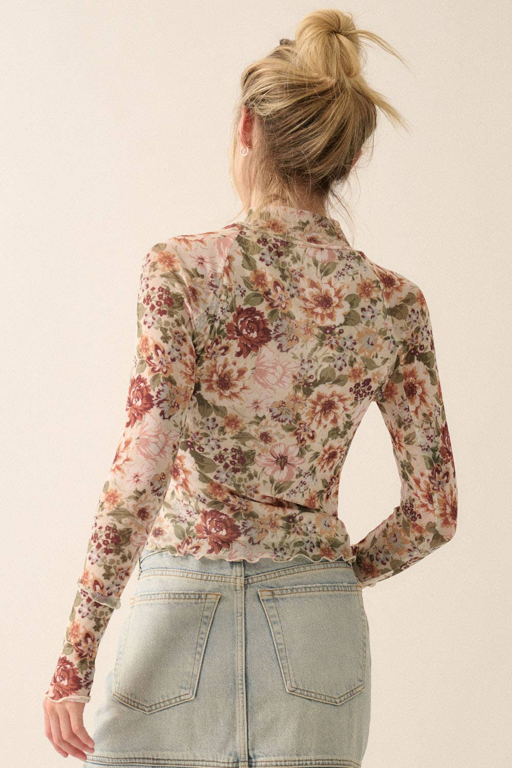 Woman wearing a sheer mesh floral long-sleeve top with mock neck and fitted silhouette.