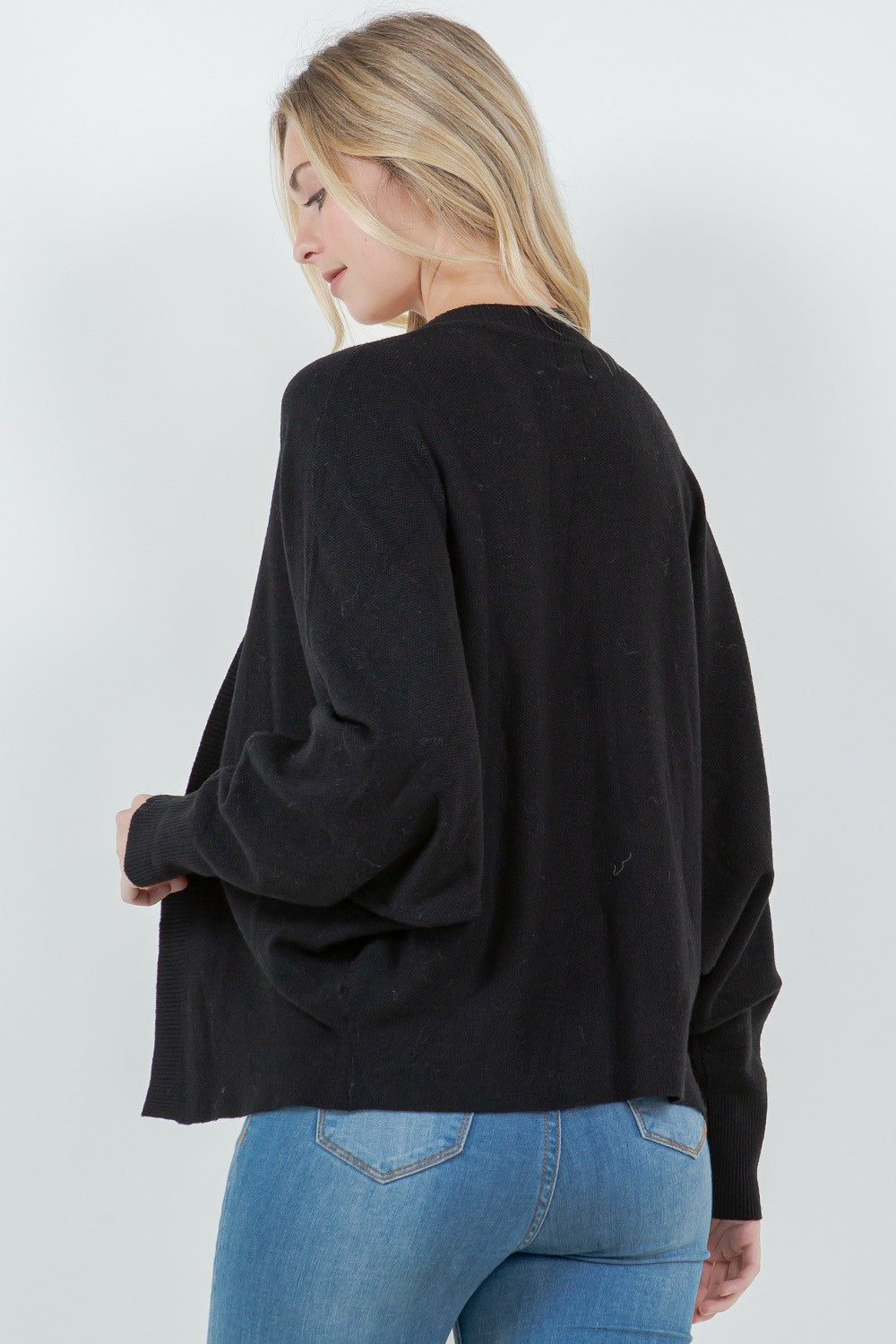 Woman wearing a black open-front cardigan with ribbed trim.