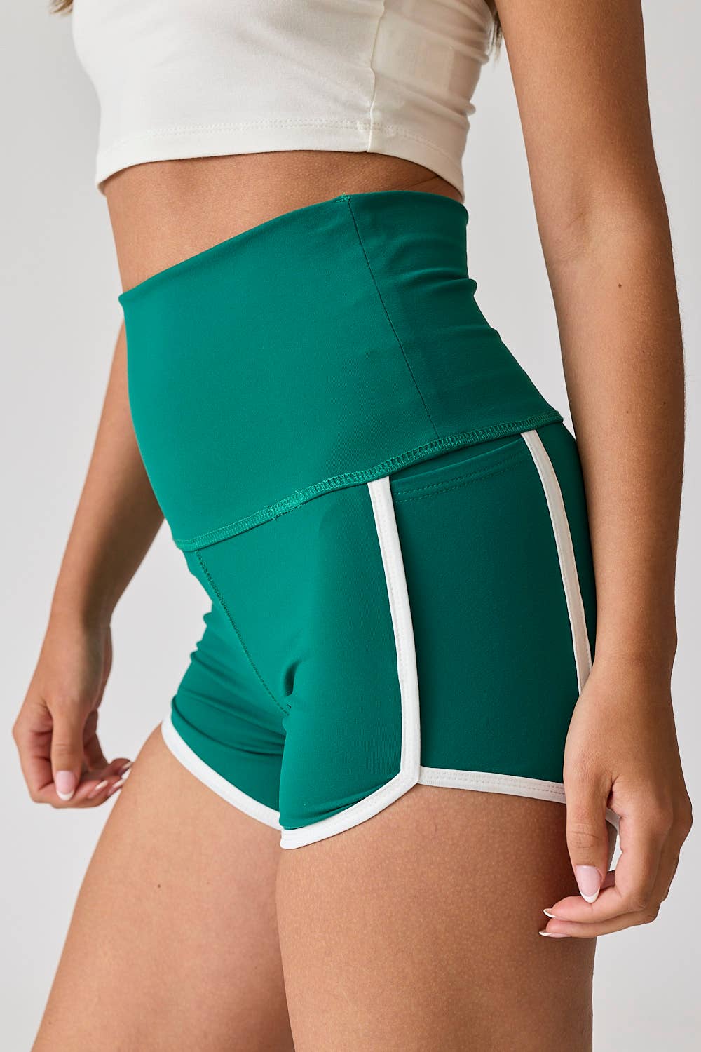 Woman wearing high-waist red shorts with white contrast piping. / Woman wearing high-waist green shorts with white contrast piping.