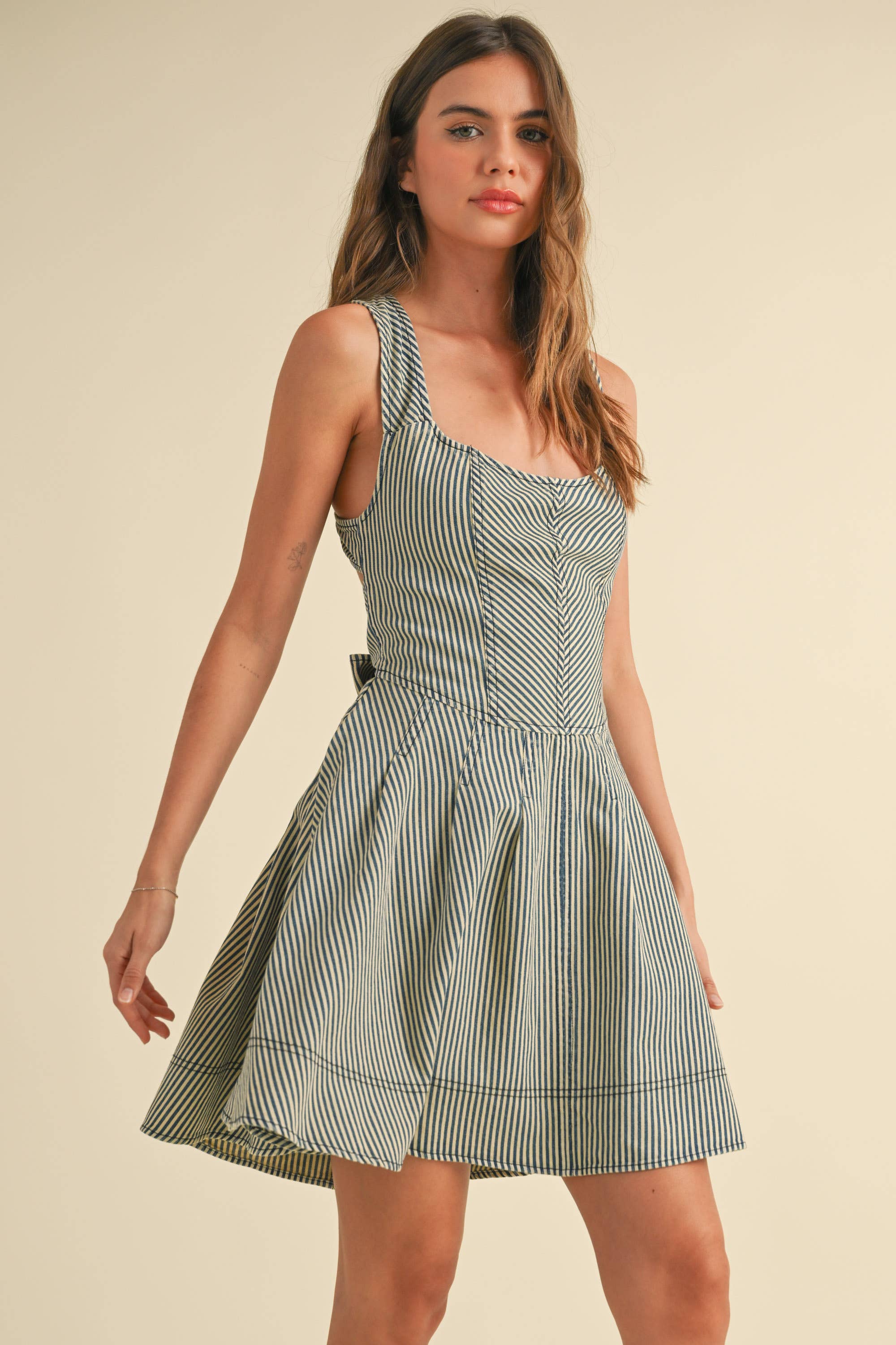 Woman wearing a sleeveless striped mini dress with criss-cross back straps and a large bow tie at the waist.
