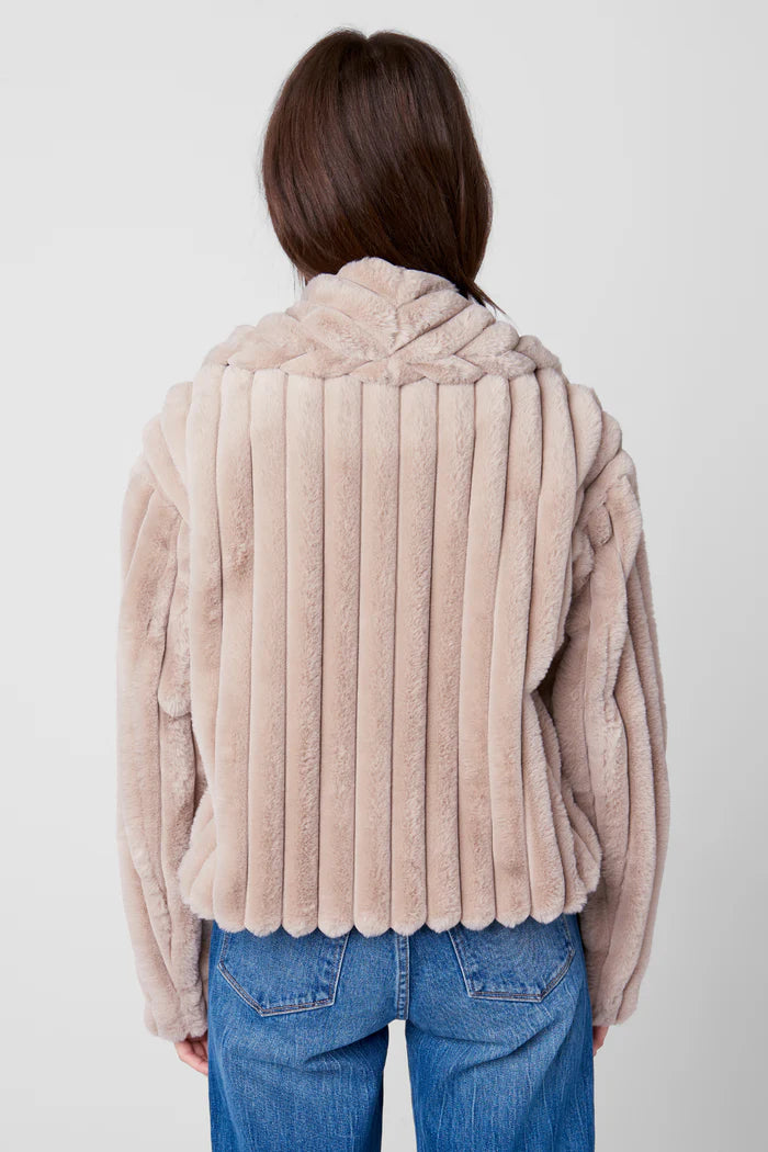 Person wearing a beige faux fur jacket and blue jeans on a white background