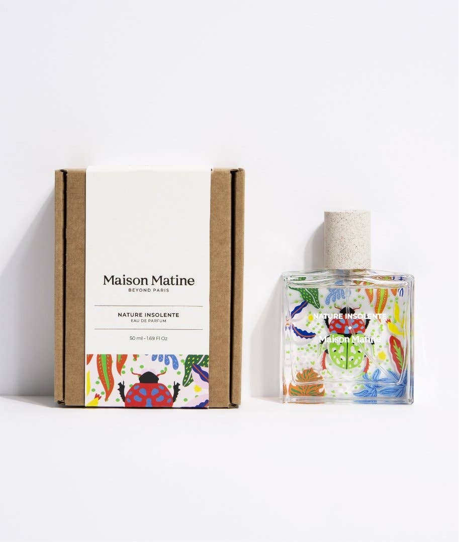 Maison Matine Nature Insolente perfume bottle with colorful leaf and beetle illustrations, placed on a vibrant yellow fabric and surrounded by green foliage.