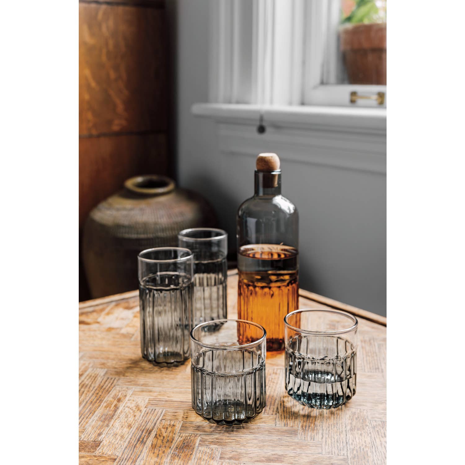 Set of glass tumblers on a wooden table with a bottle of amber liquid.