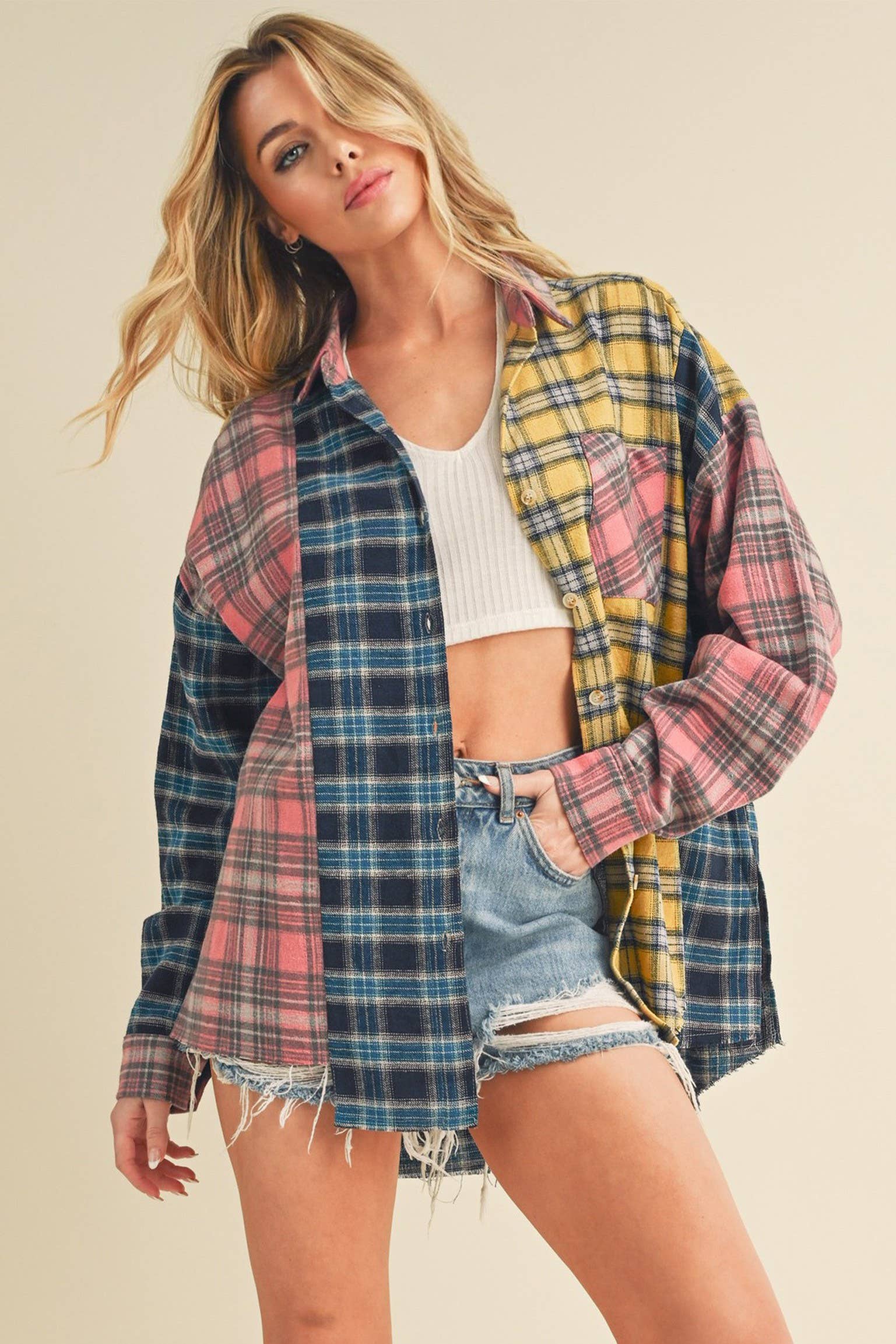 Woman wearing an oversized plaid colorblock flannel shirt in pink, yellow, and navy tones with raw hems.