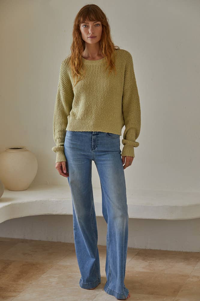 Woman wearing a cream chunky knit pullover sweater with relaxed fit, styled casually with light-wash jeans.