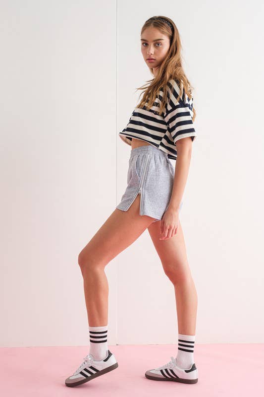 Close-up of a woman wearing gray elastic waist shorts with side zipper details.