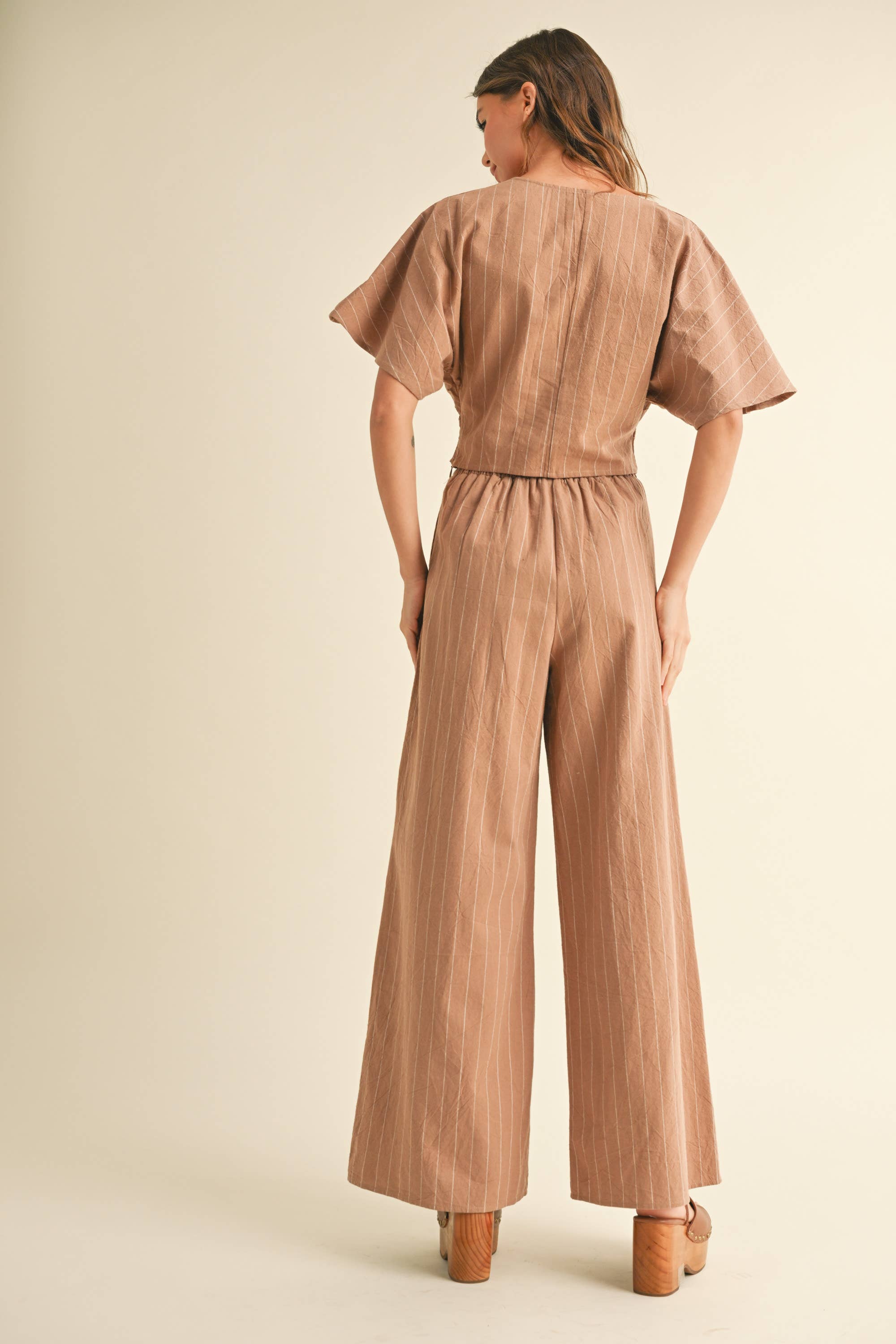 Woman wearing a two-piece striped set with a twist-front crop top and wide-leg pants in cream and tan color options.