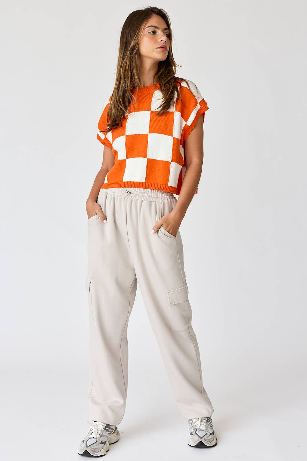 Woman wearing an orange and white loose-fit checker knit top with beige pants.