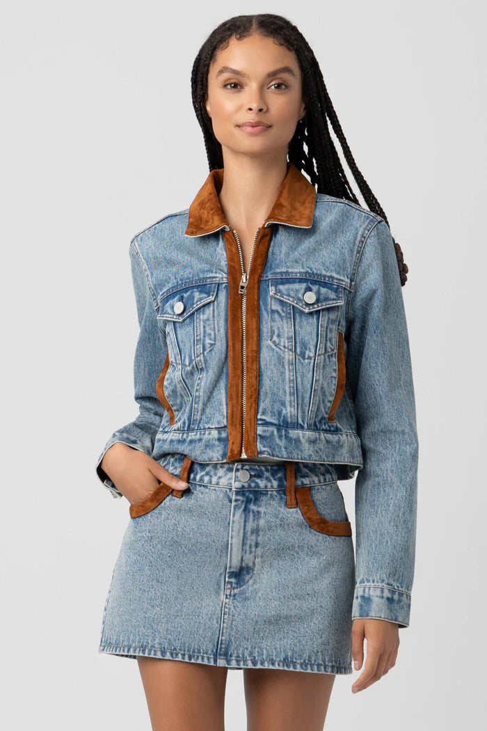 Woman wearing a denim jacket with brown interior and matching skirt on a light gray background