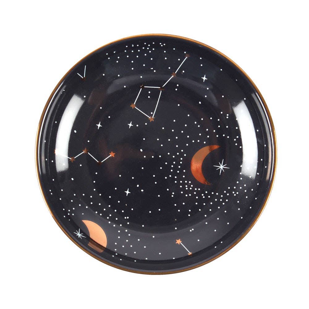 A round ceramic jewelry dish with a celestial design, including golden moons, stars, and constellations on a dark background.