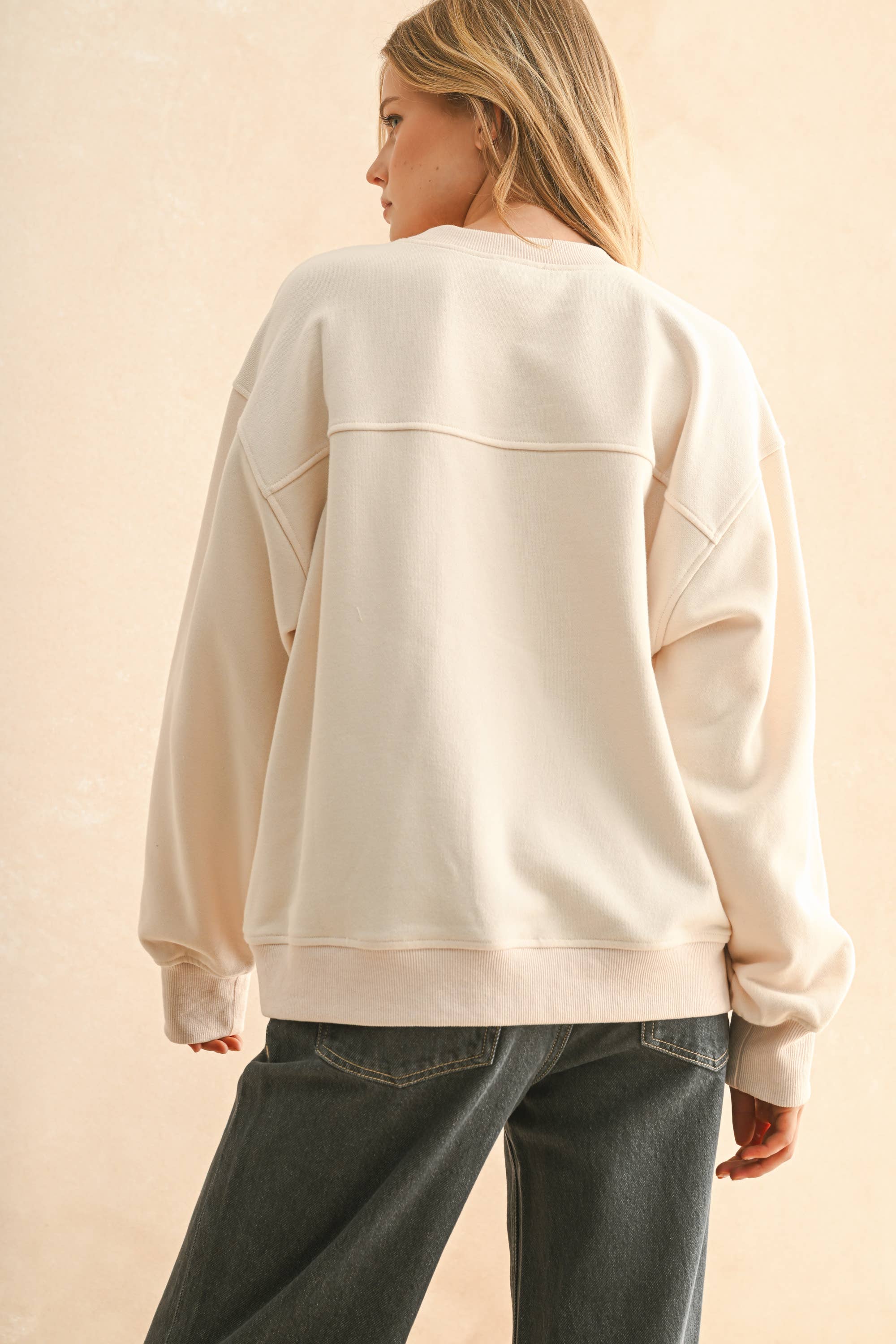 Woman wearing a cream sweater with bold red embroidered “Paris” lettering, paired with dark denim jeans.