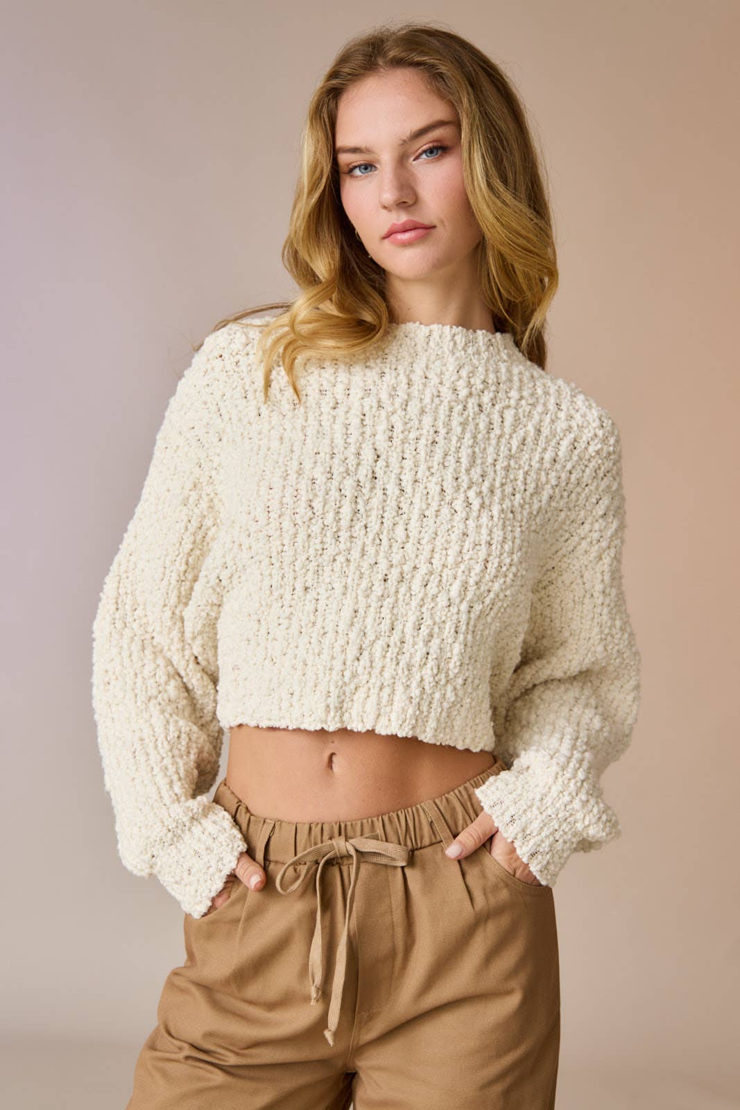 Woman wearing a cream popcorn knit cropped sweater with tan drawstring pants, hands in pockets.