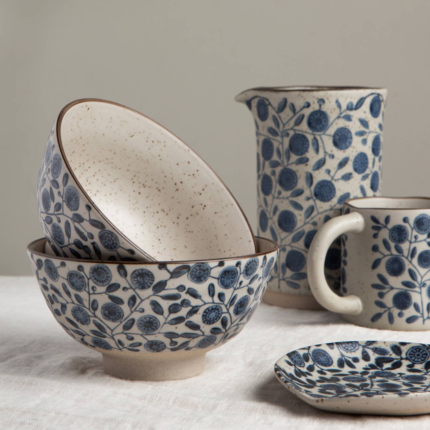 Ceramic bowls, pitcher, and mug with blue floral pattern on a neutral background