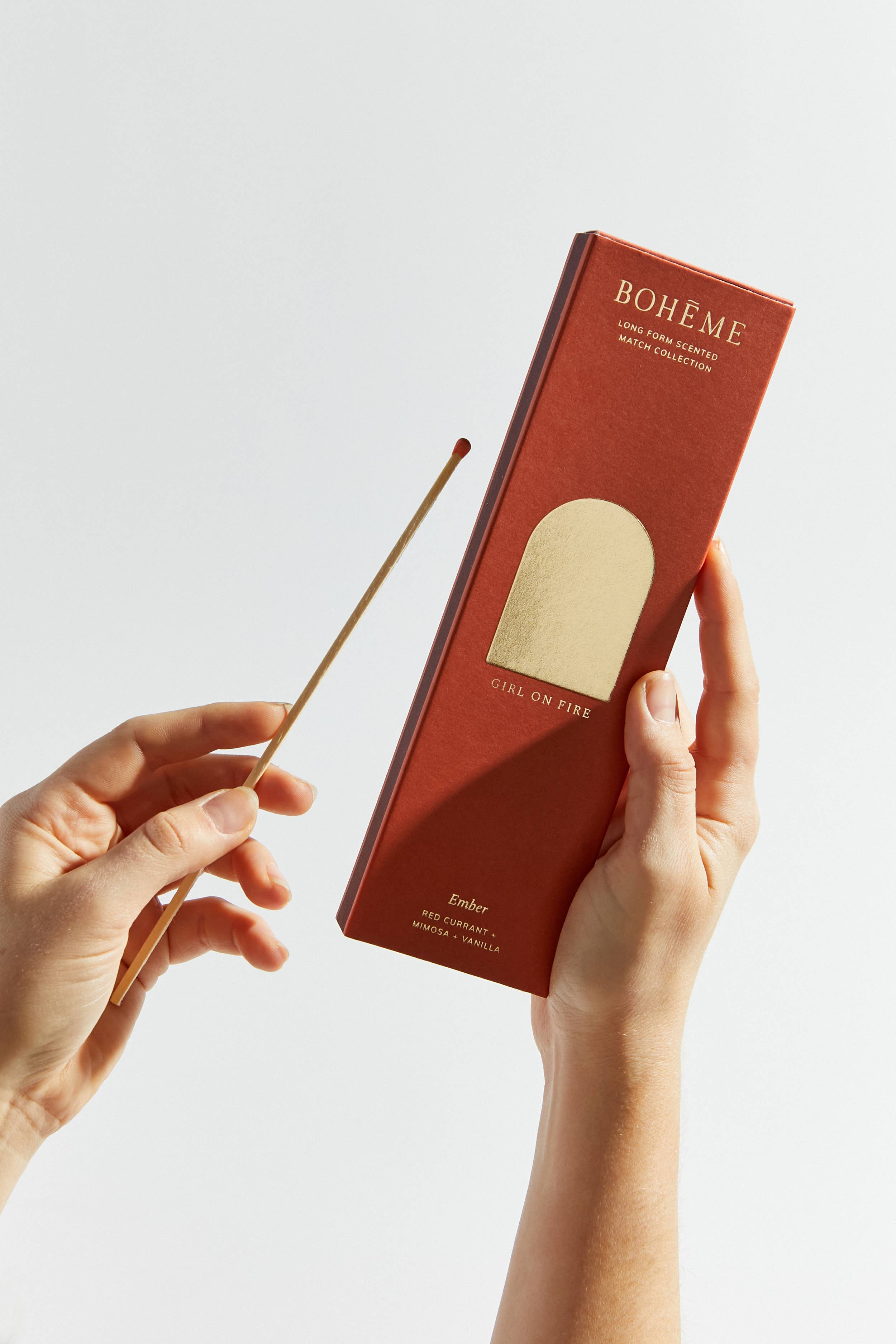 Person holding a red incense box and a single incense stick against a plain background.