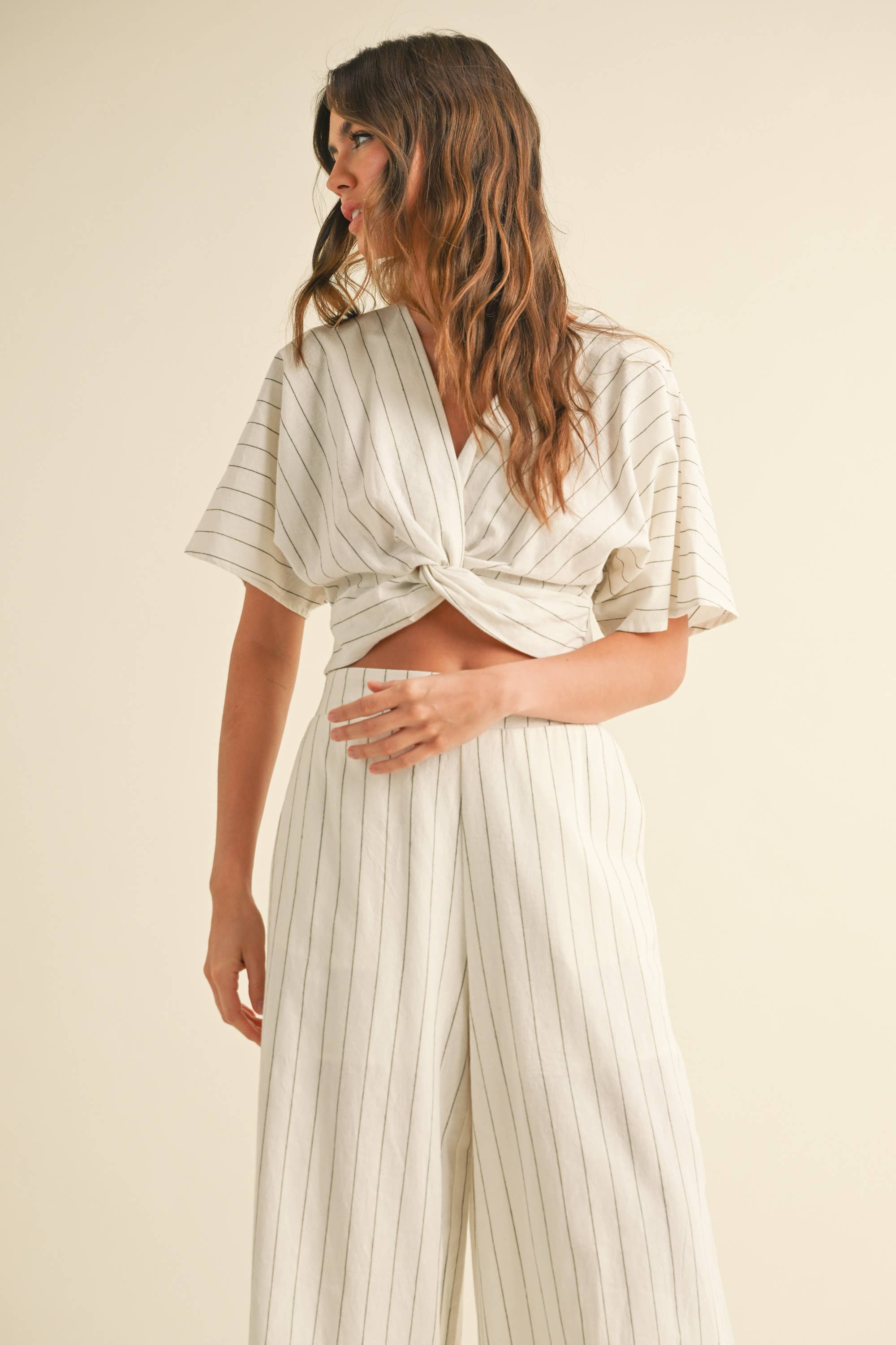 Woman wearing a two-piece striped set with a twist-front crop top and wide-leg pants in cream and tan color options.