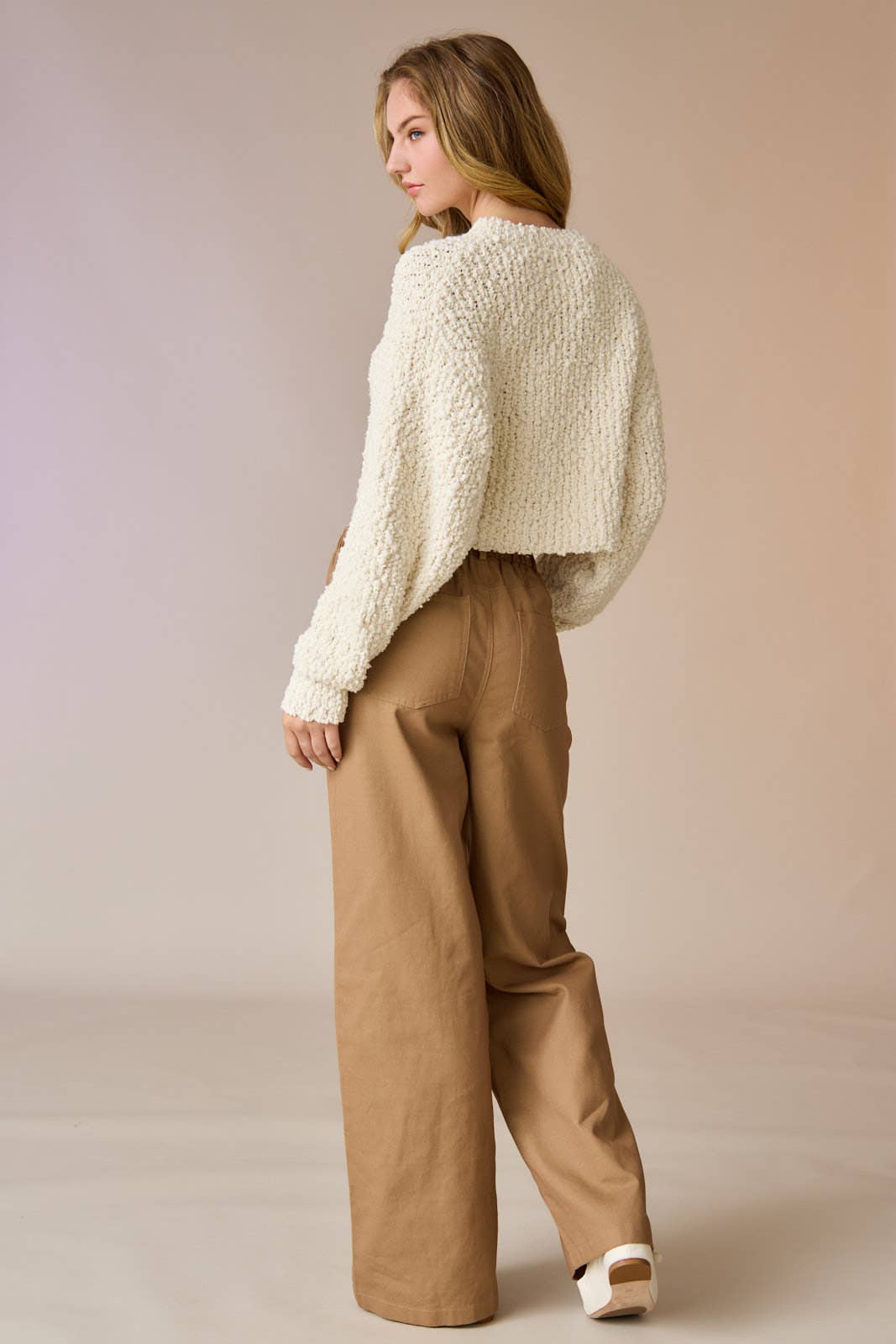 Woman wearing a cream popcorn knit cropped sweater with tan drawstring pants, hands in pockets.