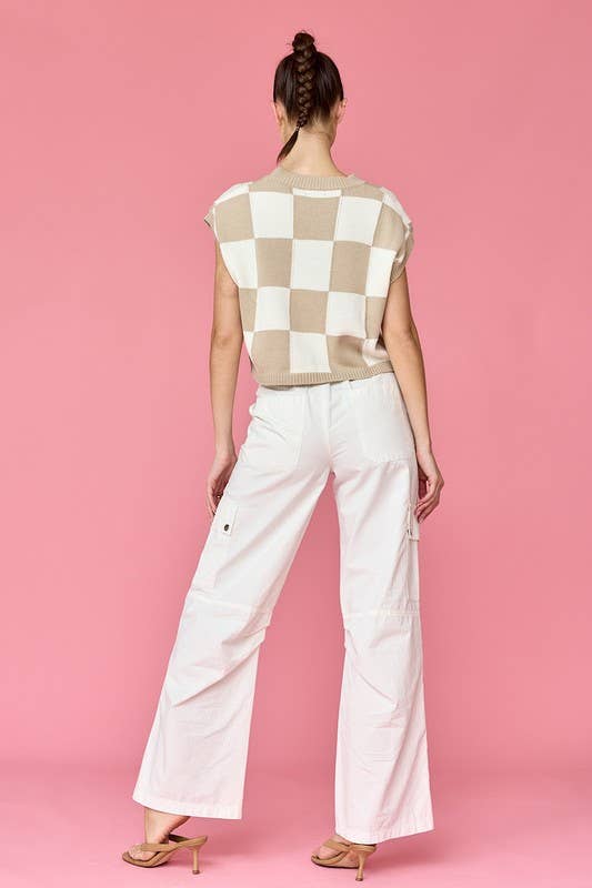 Woman wearing a taupe and white loose-fit checker knit top with white pants.