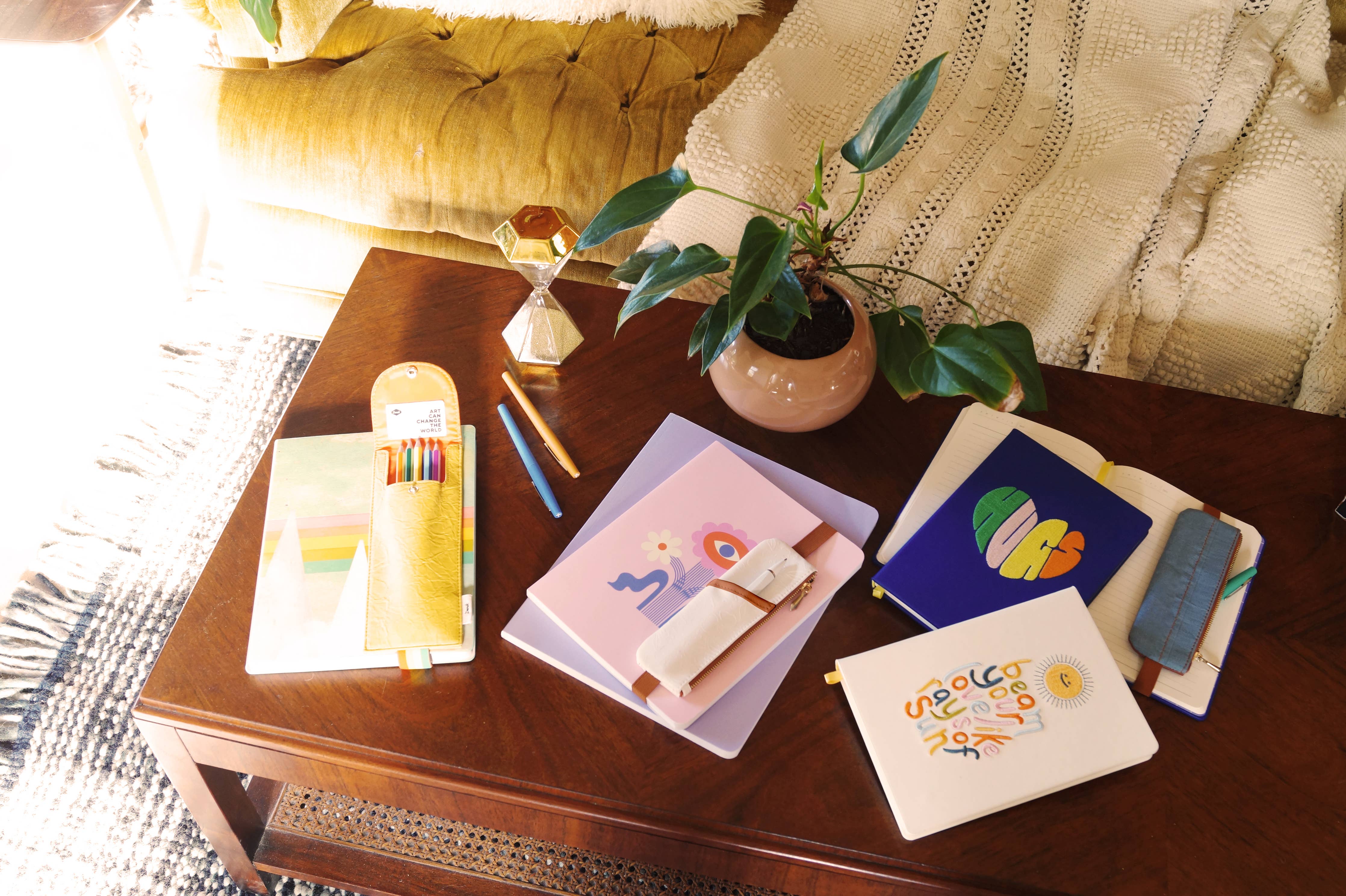 A white vegan leather notebook pouch with an embossed floral design, tan accents, and a gold zipper, attached to its packaging.