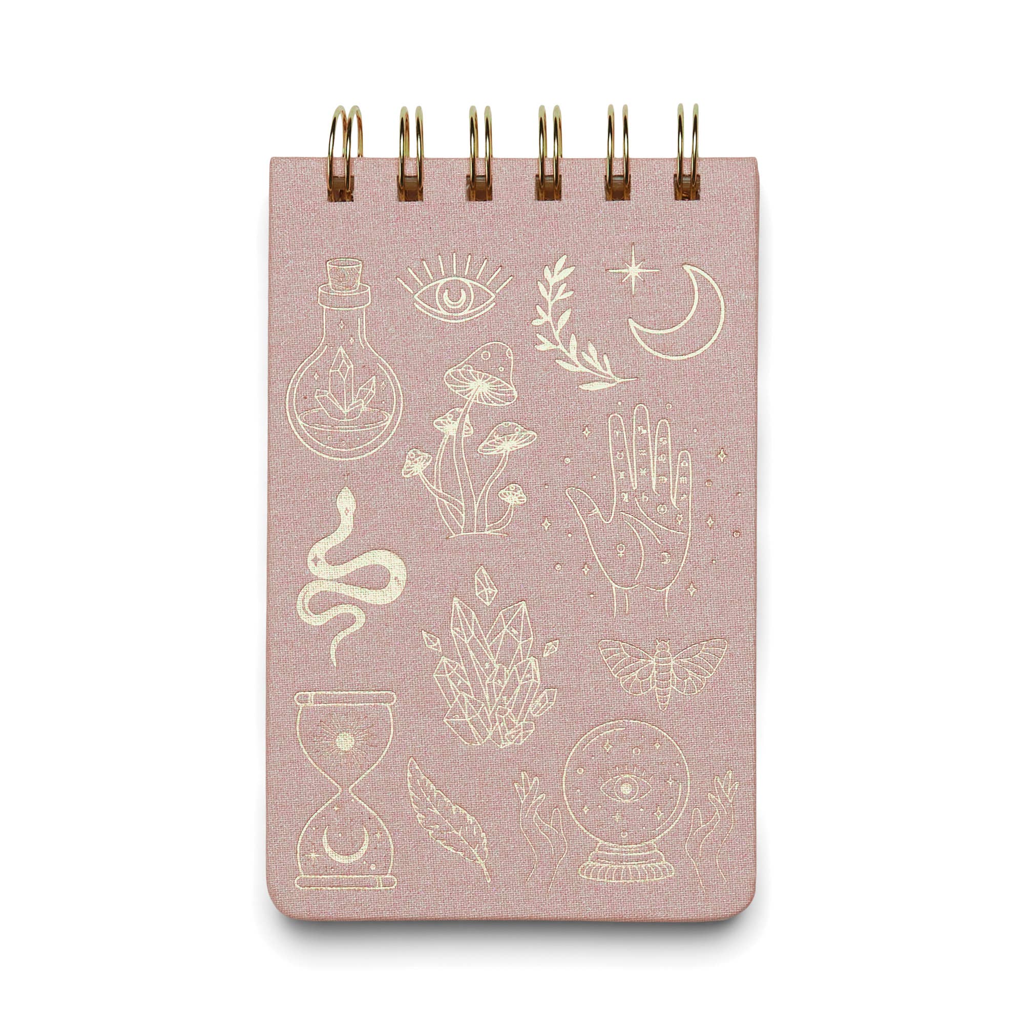 A pink cloth-covered notepad with a gold foil spiral binding and various gold foil accents on the cover, including symbols such as eyes, leaves, and celestial bodies.