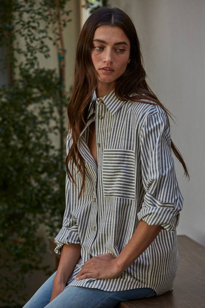 Woman wearing a long-sleeve striped button-up shirt with front pocket, styled casually with rolled cuffs and jeans.