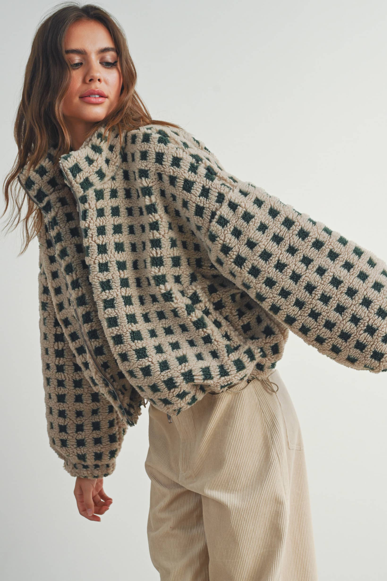 Woman wearing a beige and green checkered fleece jacket with a zip closure, paired with a white crop top and beige corduroy pants.