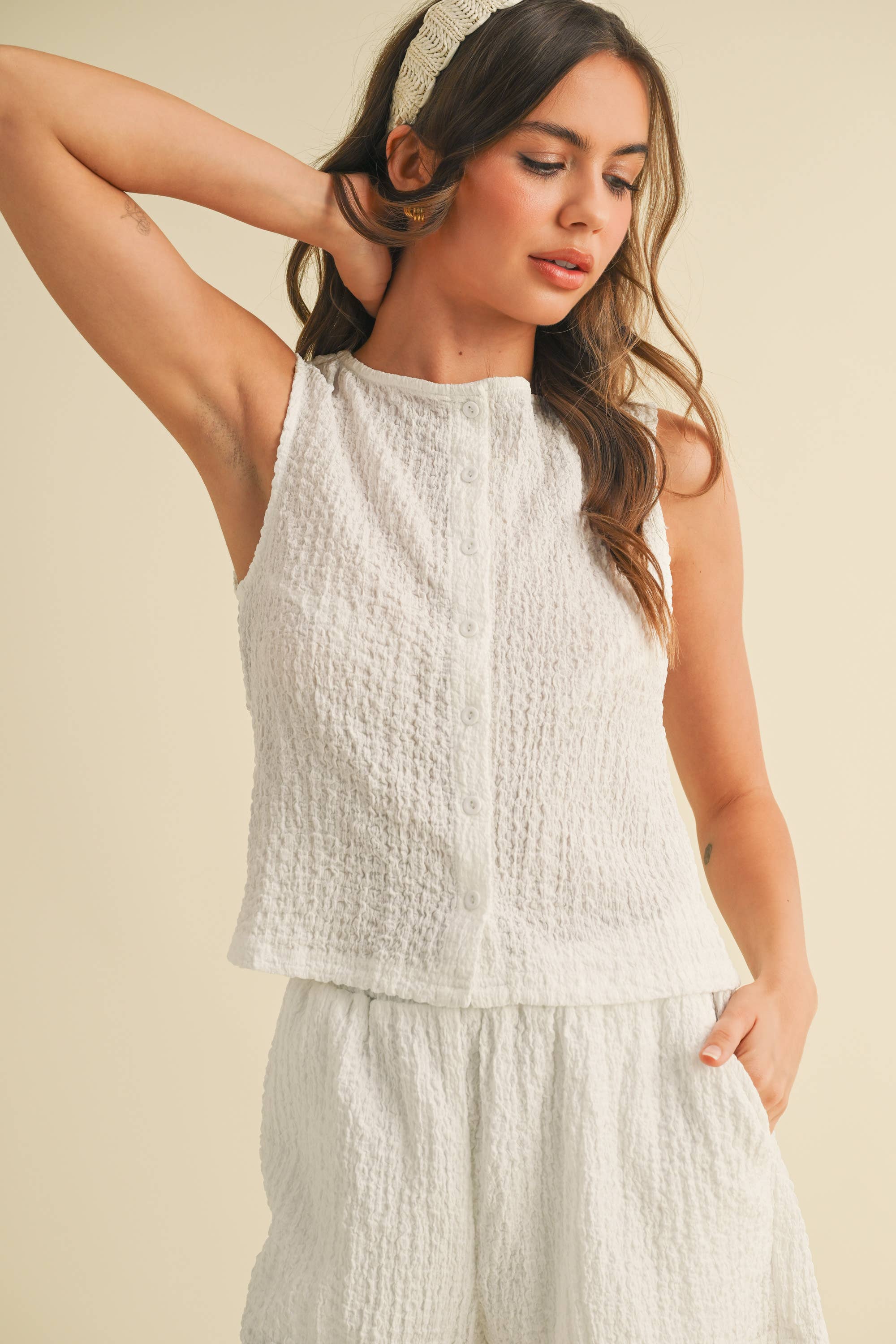 Model wearing a white sleeveless textured two-piece set featuring a cropped top and matching shorts with pockets.