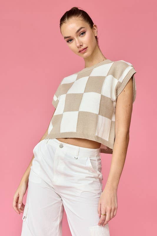 Woman wearing a taupe and white loose-fit checker knit top with white pants.
