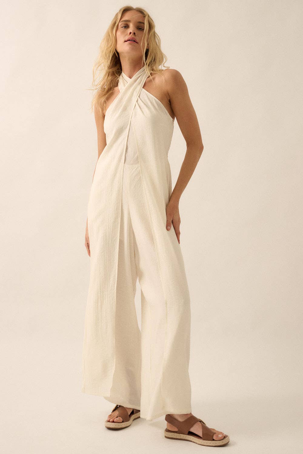 Woman wearing a white halter jumpsuit with tie-back neckline and wide-leg pants, styled with sandals.