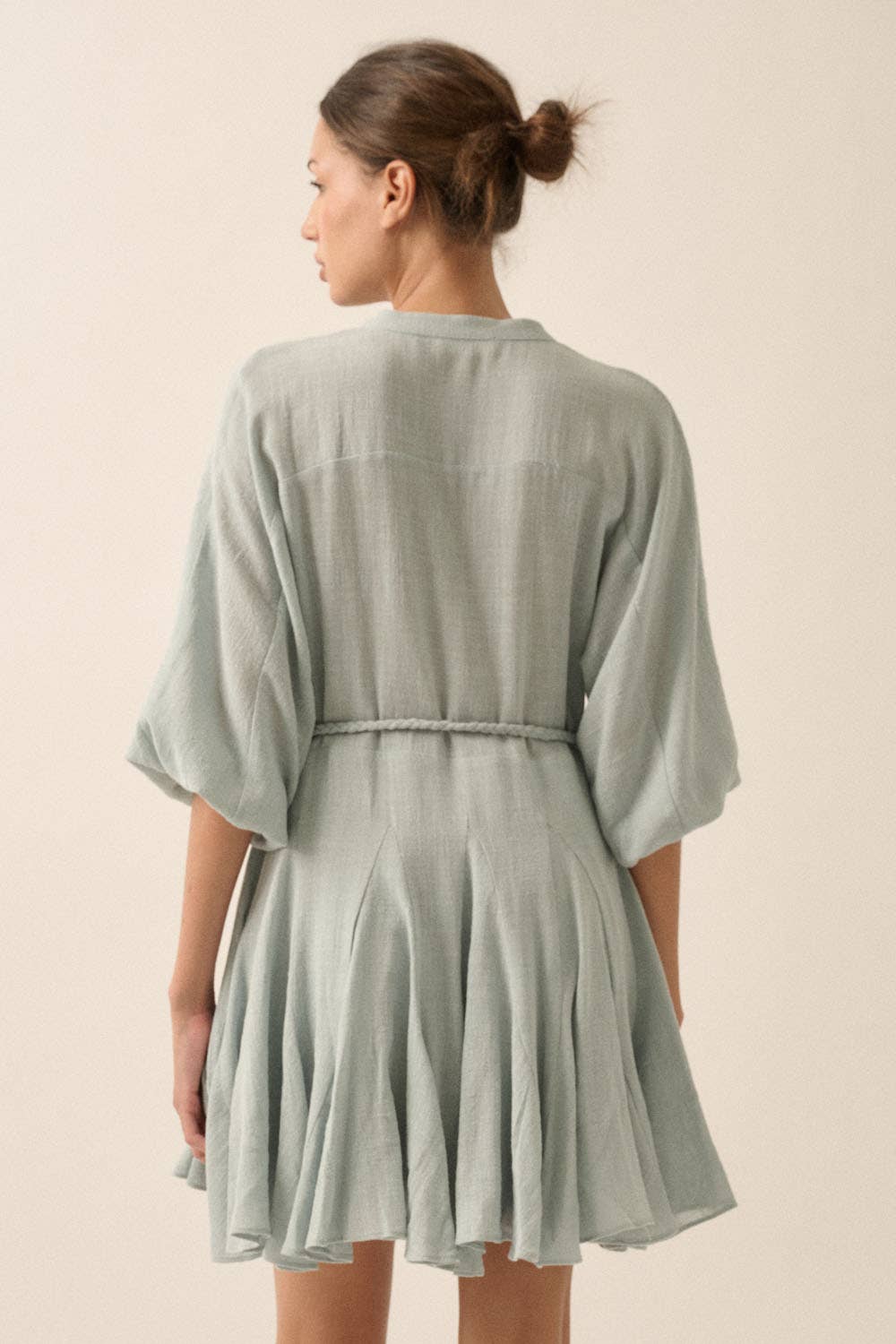 Woman wearing a sage green button-down mini dress with a braided waist tie and flowy hemline.