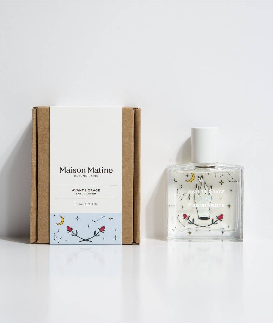 Maison Matine Avant l’Orage perfume bottle with celestial illustrations, placed among citrus fruits and sample vials on blue fabric