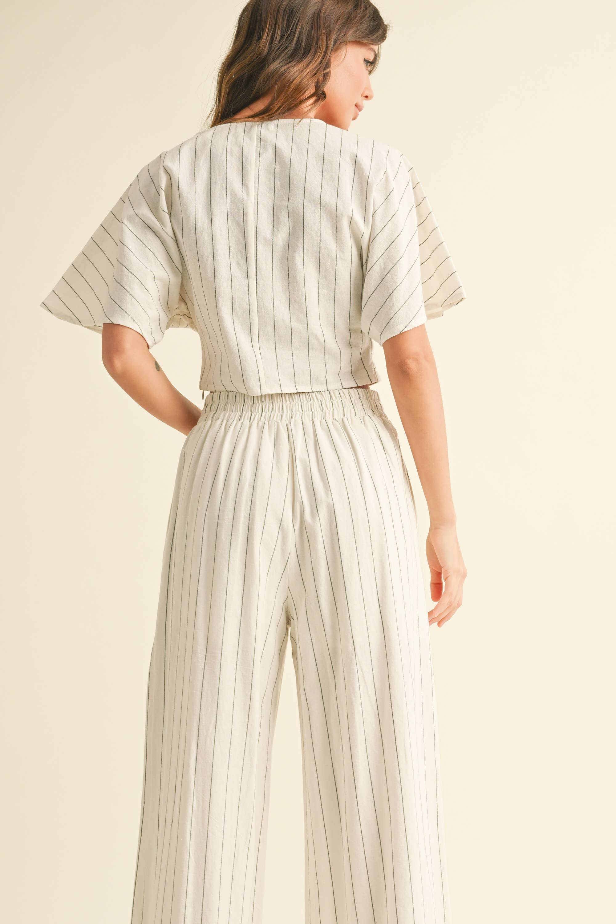 Woman wearing a two-piece striped set with a twist-front crop top and wide-leg pants in cream and tan color options.