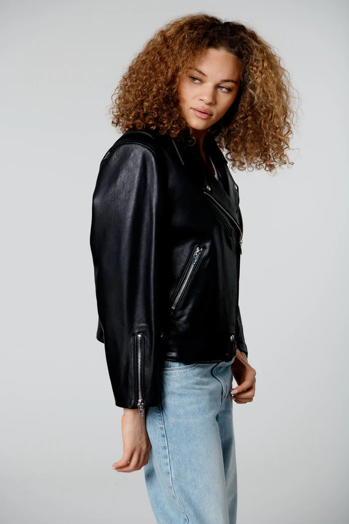 Person wearing a black leather jacket and light blue jeans on a plain background
