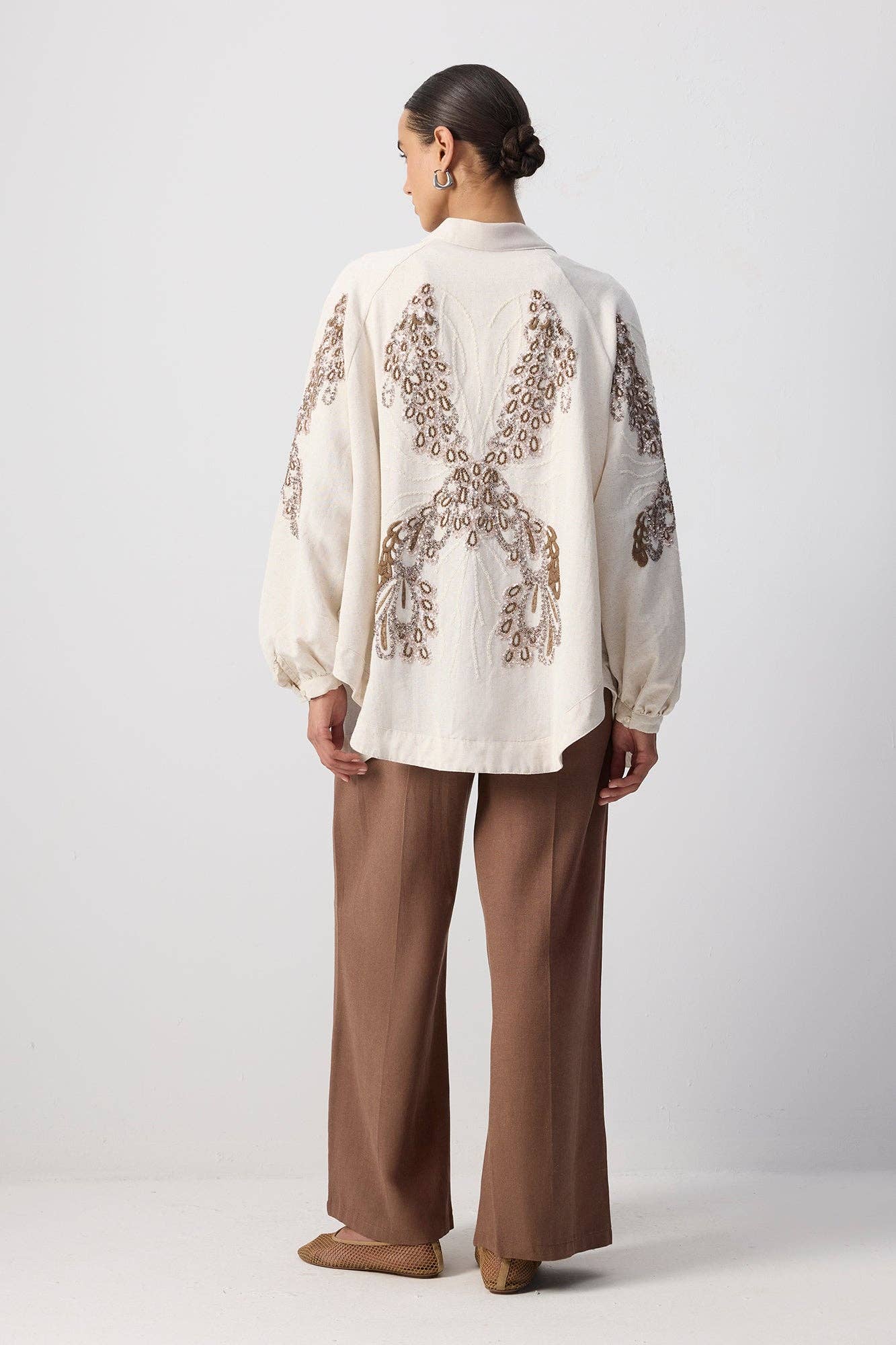 Back view of a woman wearing a cream embroidered kimono with sequin detailing and wide sleeves.