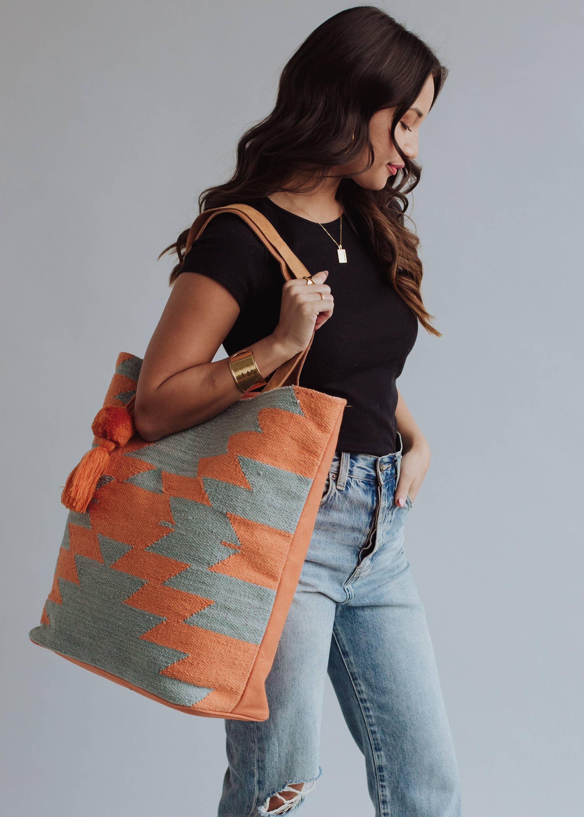 Tote bag with orange and sage green zigzag design and tassel, styled with denim jeans