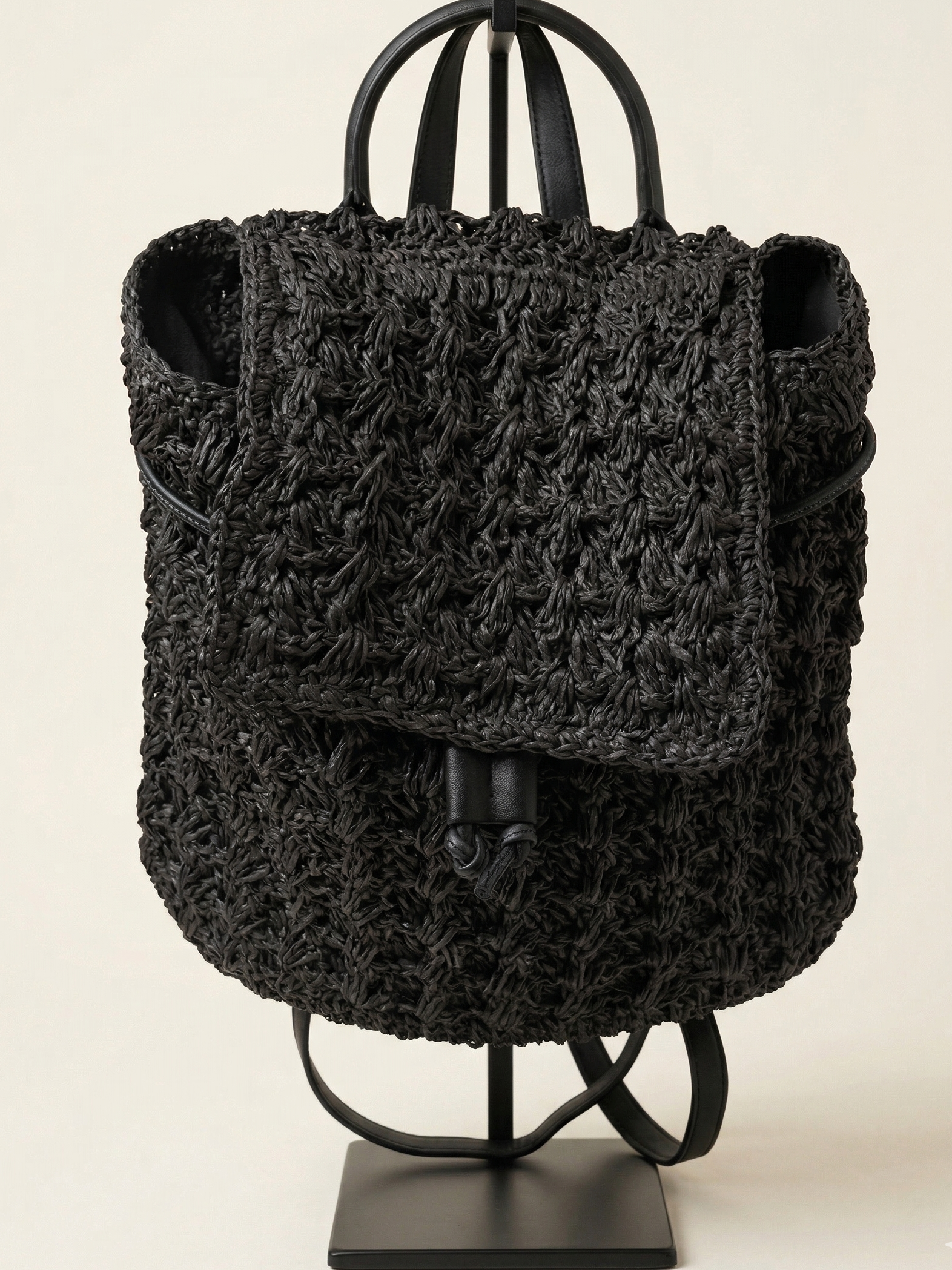 Black textured backpack on a stand against a beige background