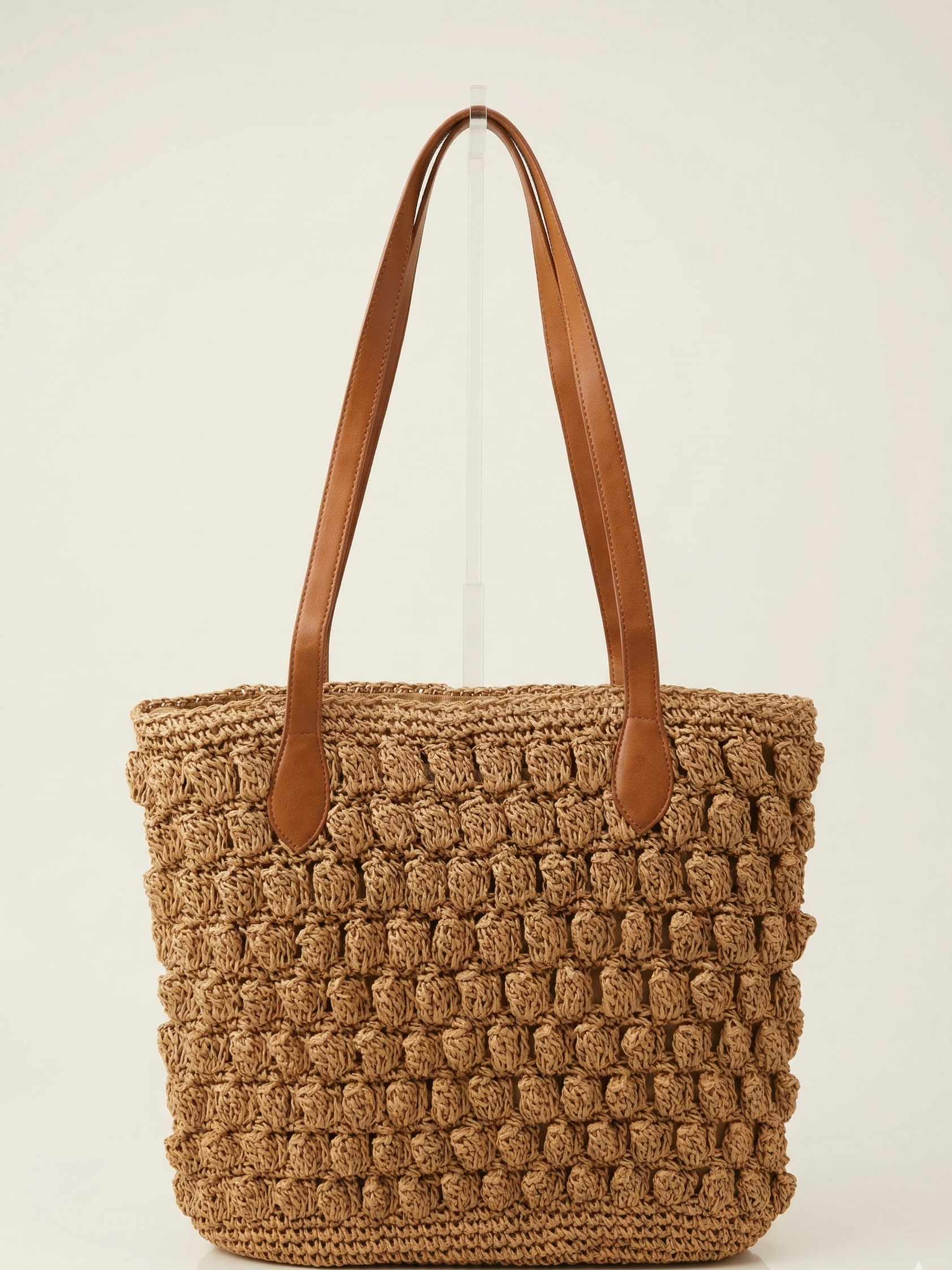 Brown woven tote bag with brown leather straps on a light beige background