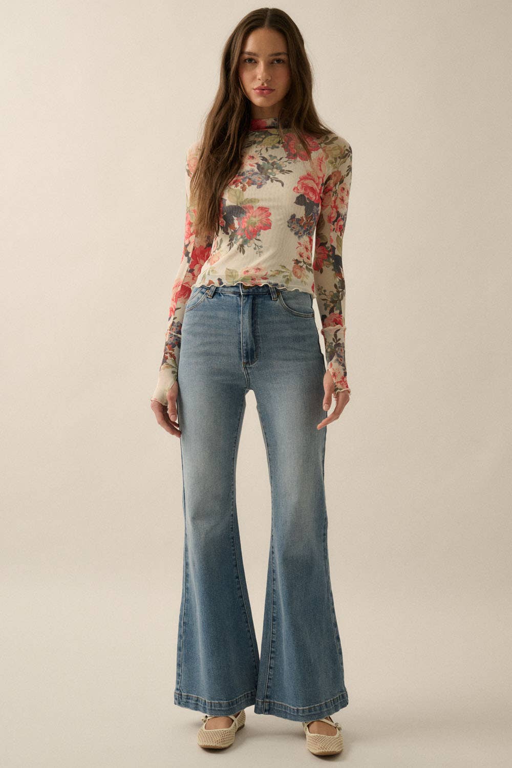 Model wearing a fitted sheer mesh long sleeve top with red, pink, and green floral print, paired with blue jeans.