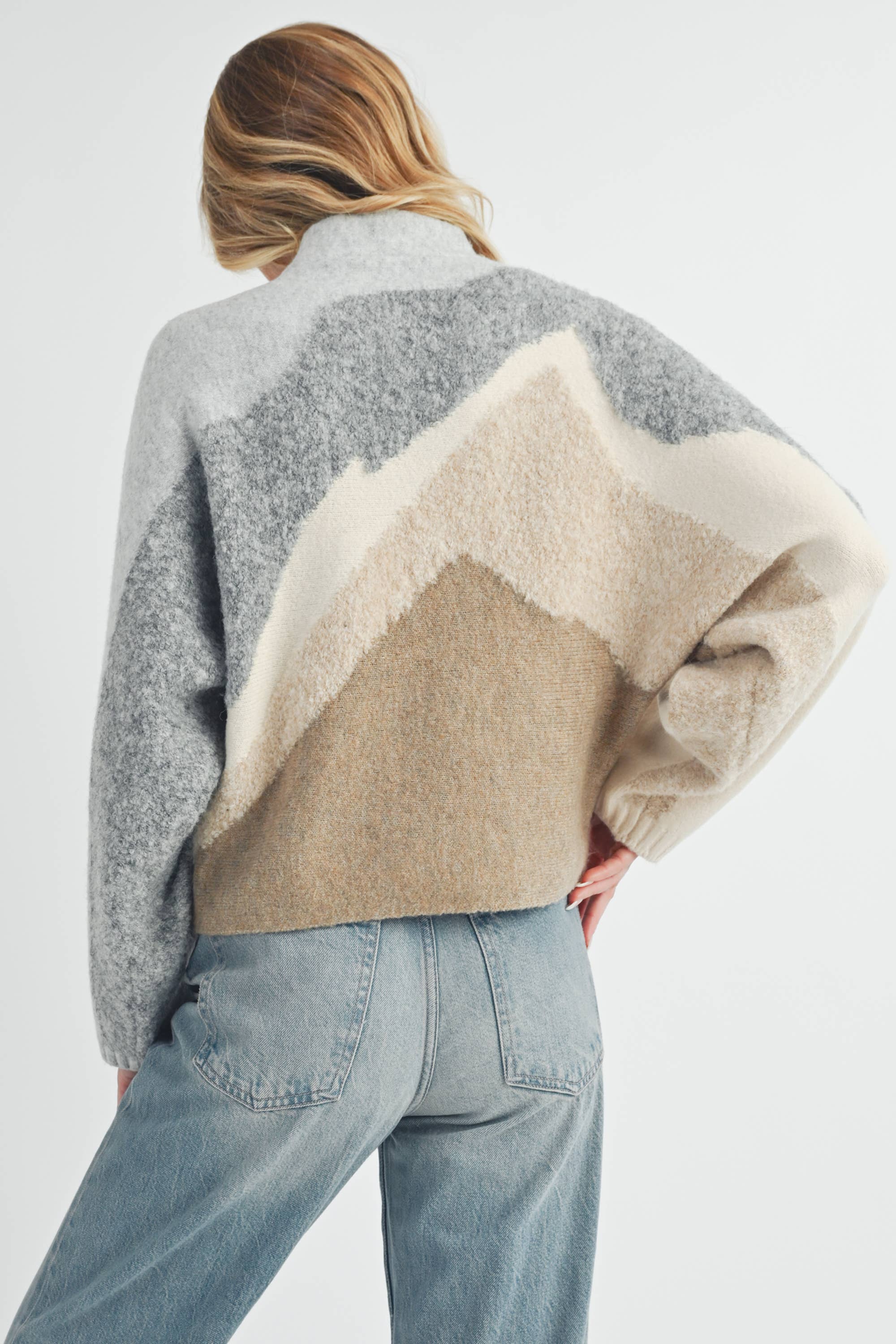 Front and back view of a woman wearing a color-block knit sweater in grey, cream, and taupe with a relaxed fit.