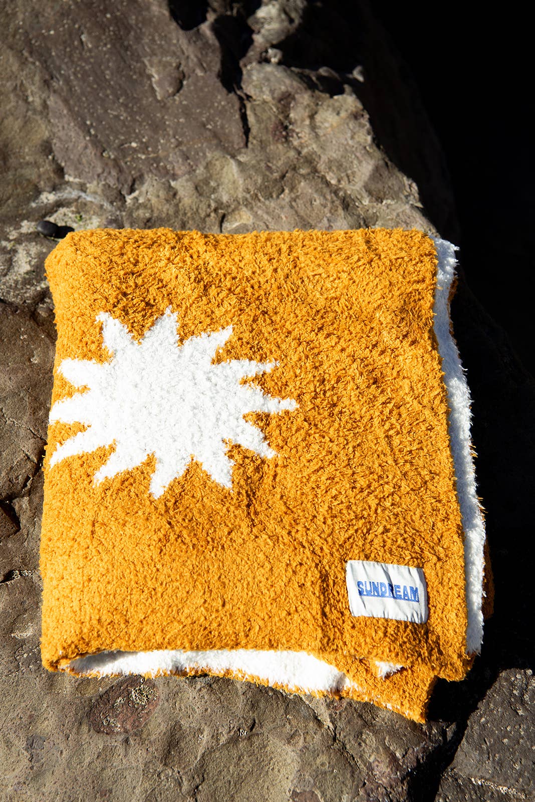 Cozy plush throw blanket in buckhorn brown with a white sunburst pattern, draped over a leather couch in a stylish and inviting living room.