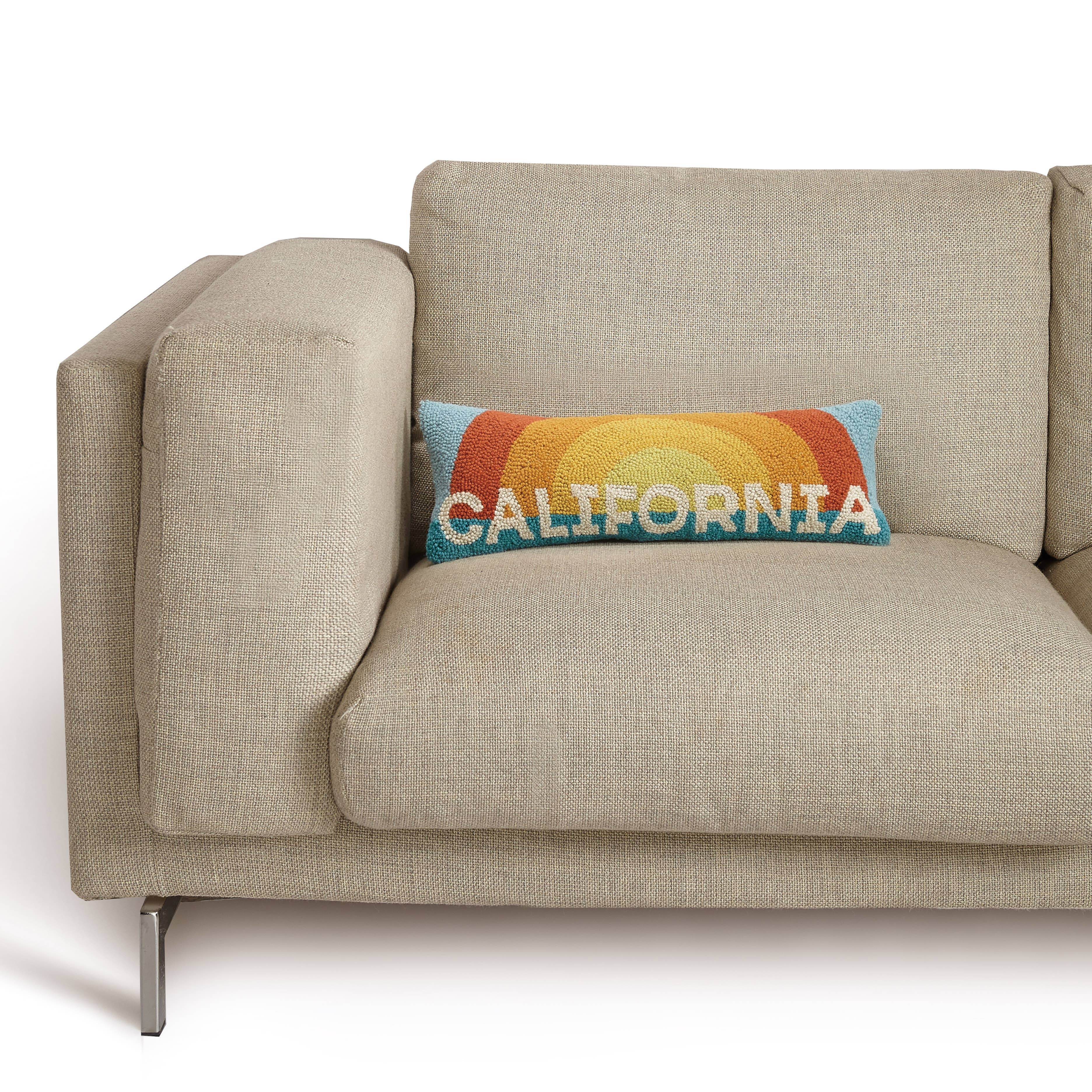 California Sun hook pillow with a retro sunburst design in orange, yellow, and blue, and "California" text in bold white letters.
