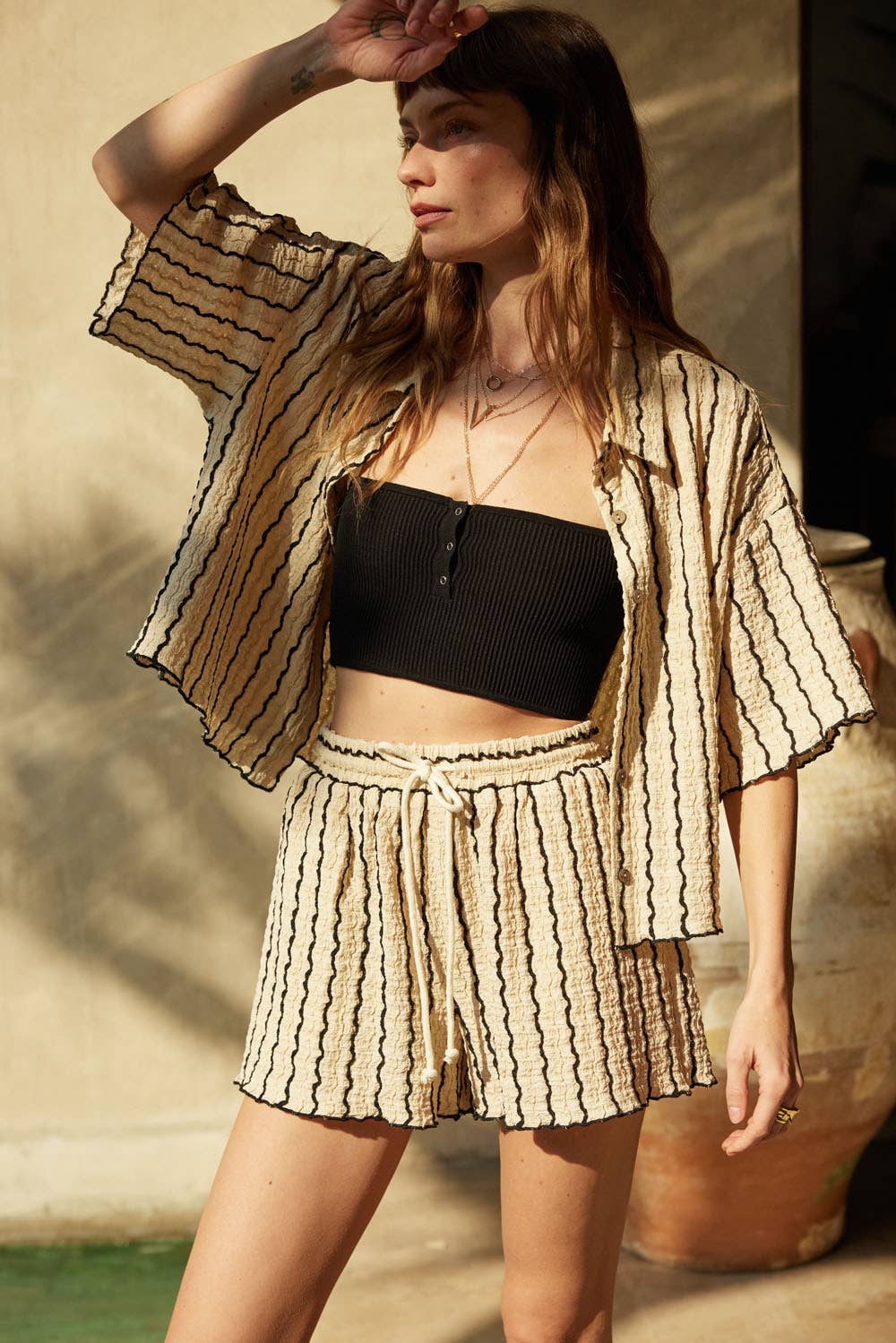 Woman wearing a beige striped two-piece lounge set with button-up shirt and matching drawstring shorts.